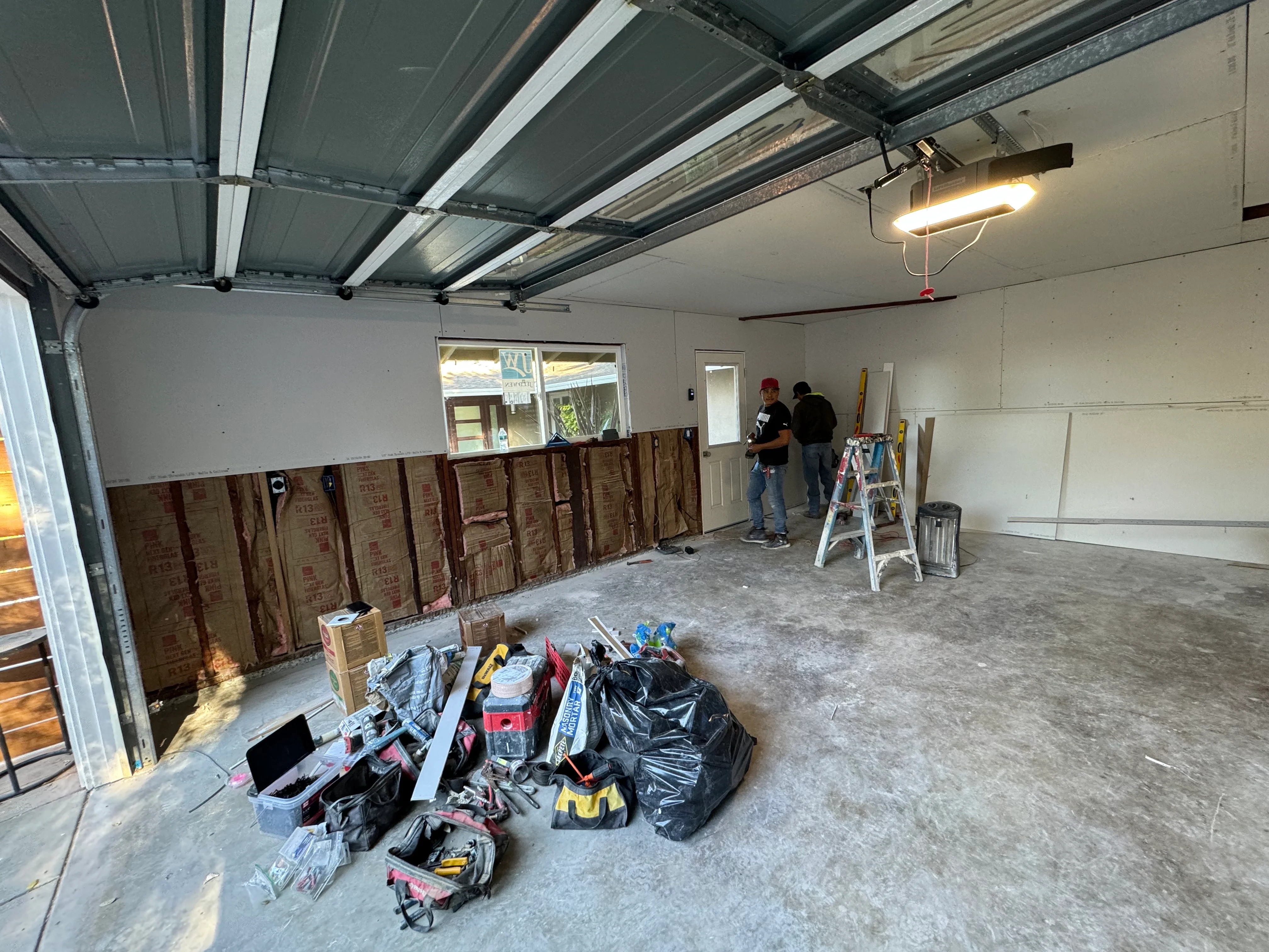 Garage interior with new drywall, metal stud framing, insulation, and LED lighting during renovation