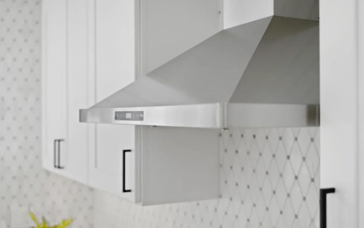 Stainless steel range hood installed above white kitchen cabinets with subway tile backsplash