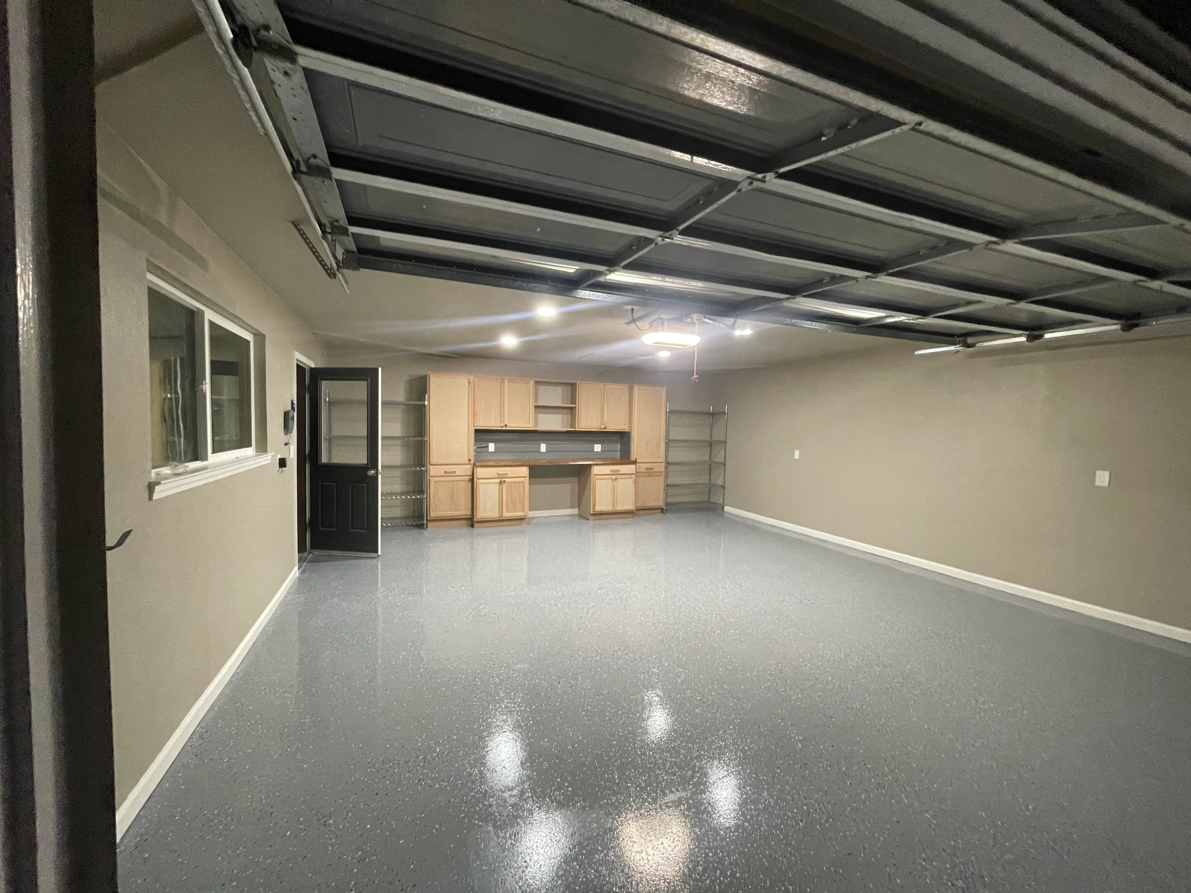 Finished garage with gray epoxy floor, beige walls, wood cabinetry, and metal overhead storage system