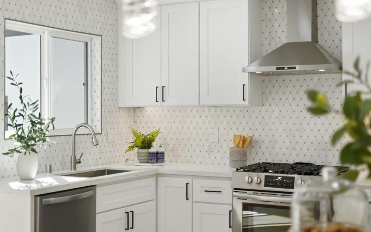 White kitchen with quartz counters, geometric tile backsplash, stainless steel appliances, and custom cabinetry