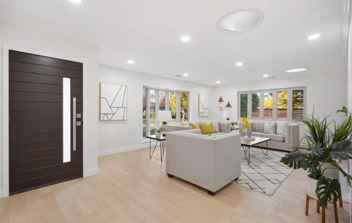 Open-concept living room with recessed lighting, white walls, light wood floors, and glass doors