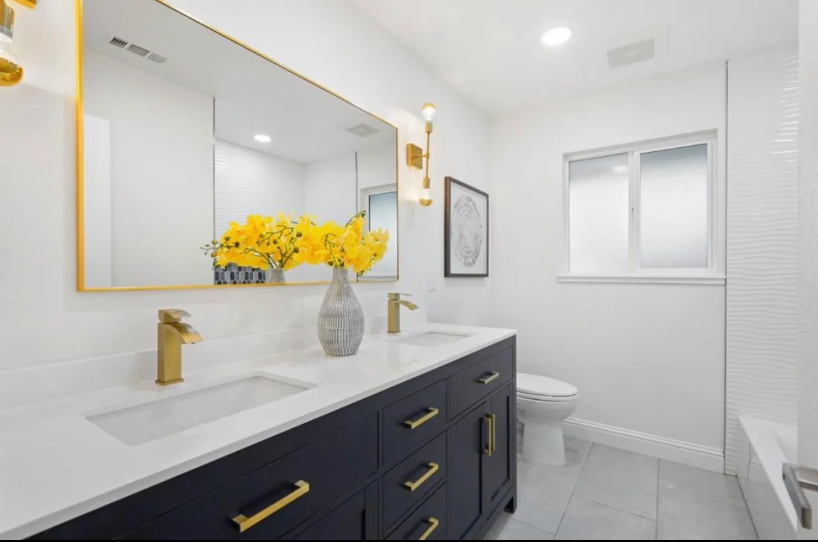 Modern bathroom with dark vanity, white quartz counters, brass fixtures, and subway tile walls