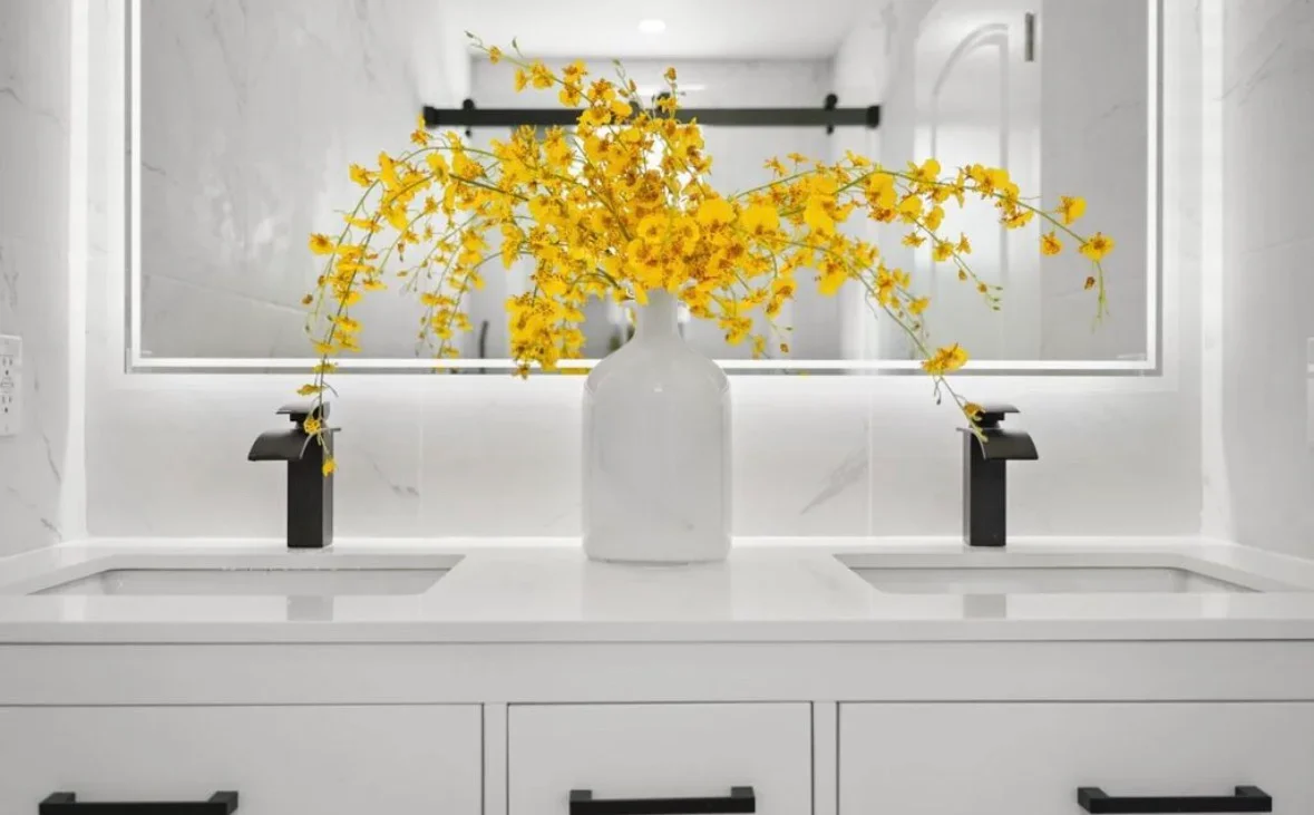 Modern bathroom vanity with white quartz countertop, dual black faucets, and large framed mirror