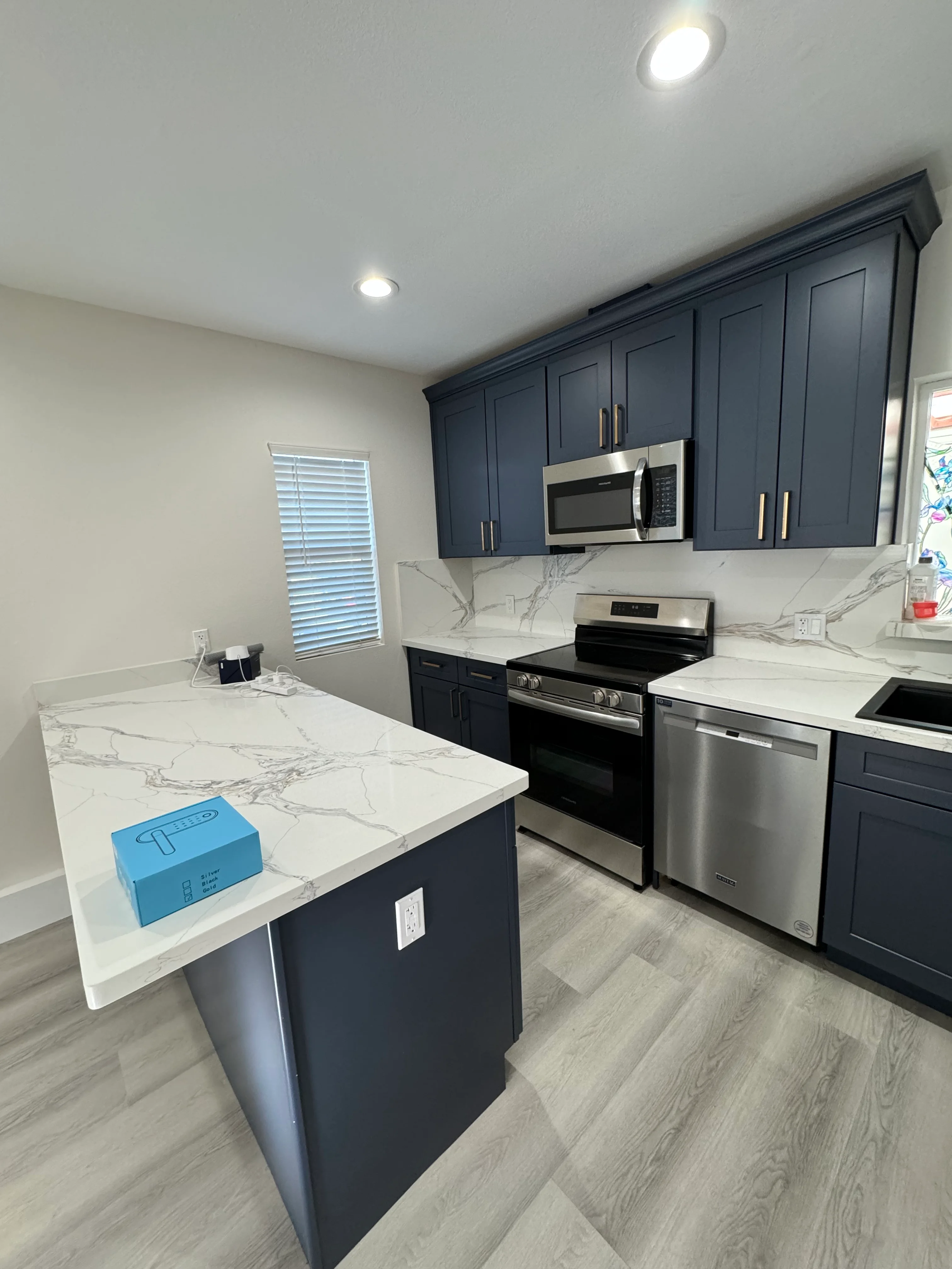 Dark blue cabinetry, marble countertops, stainless steel appliances, and island in modern kitchen