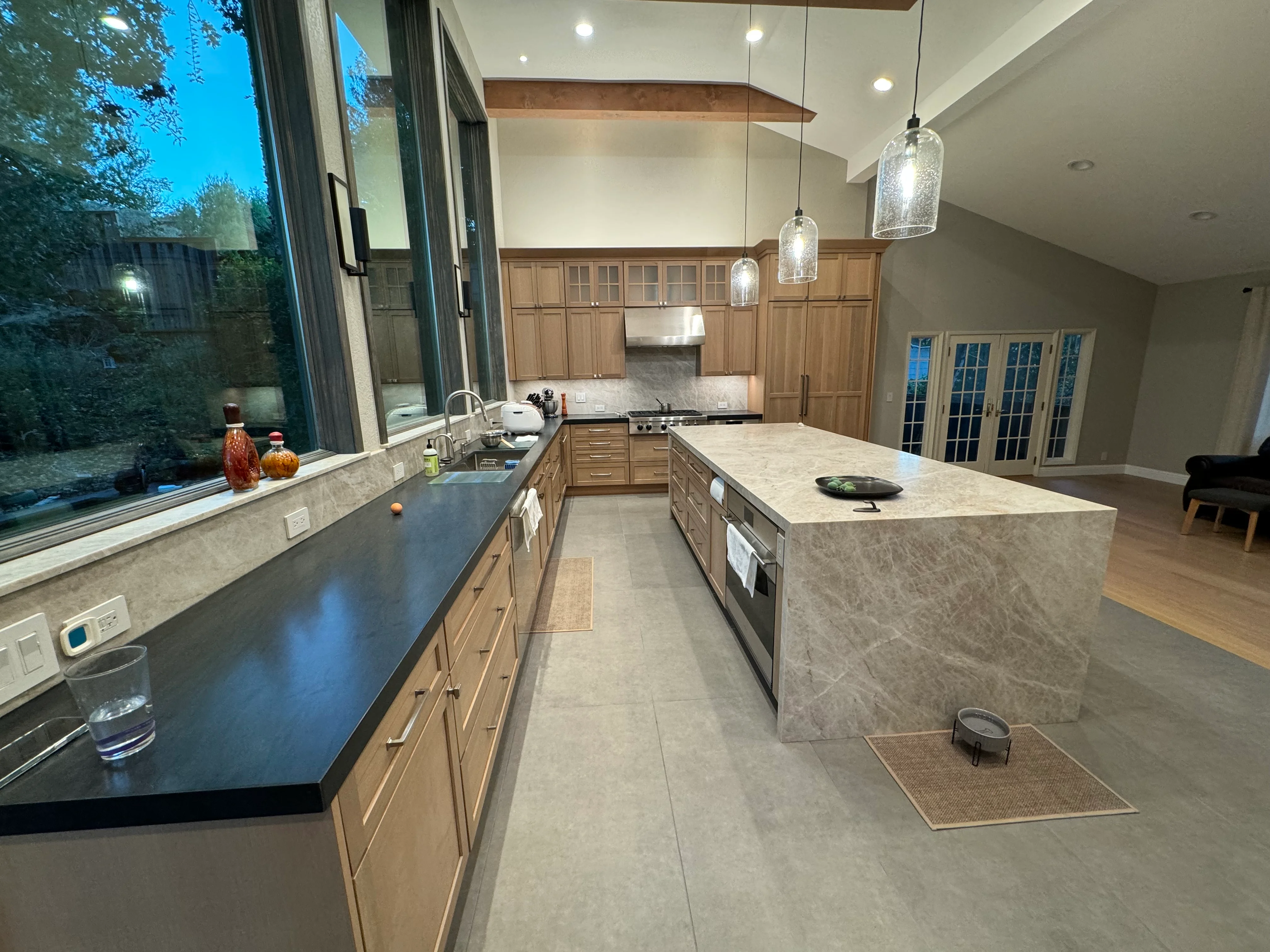 Kitchen with wood cabinetry, quartz counters, waterfall island, stainless appliances, pendant lights