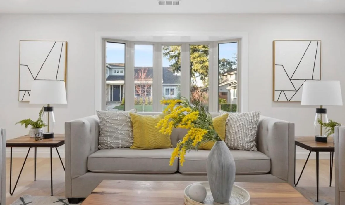 Modern living room with gray sofa, yellow accents, wood tables, and multi-panel windows