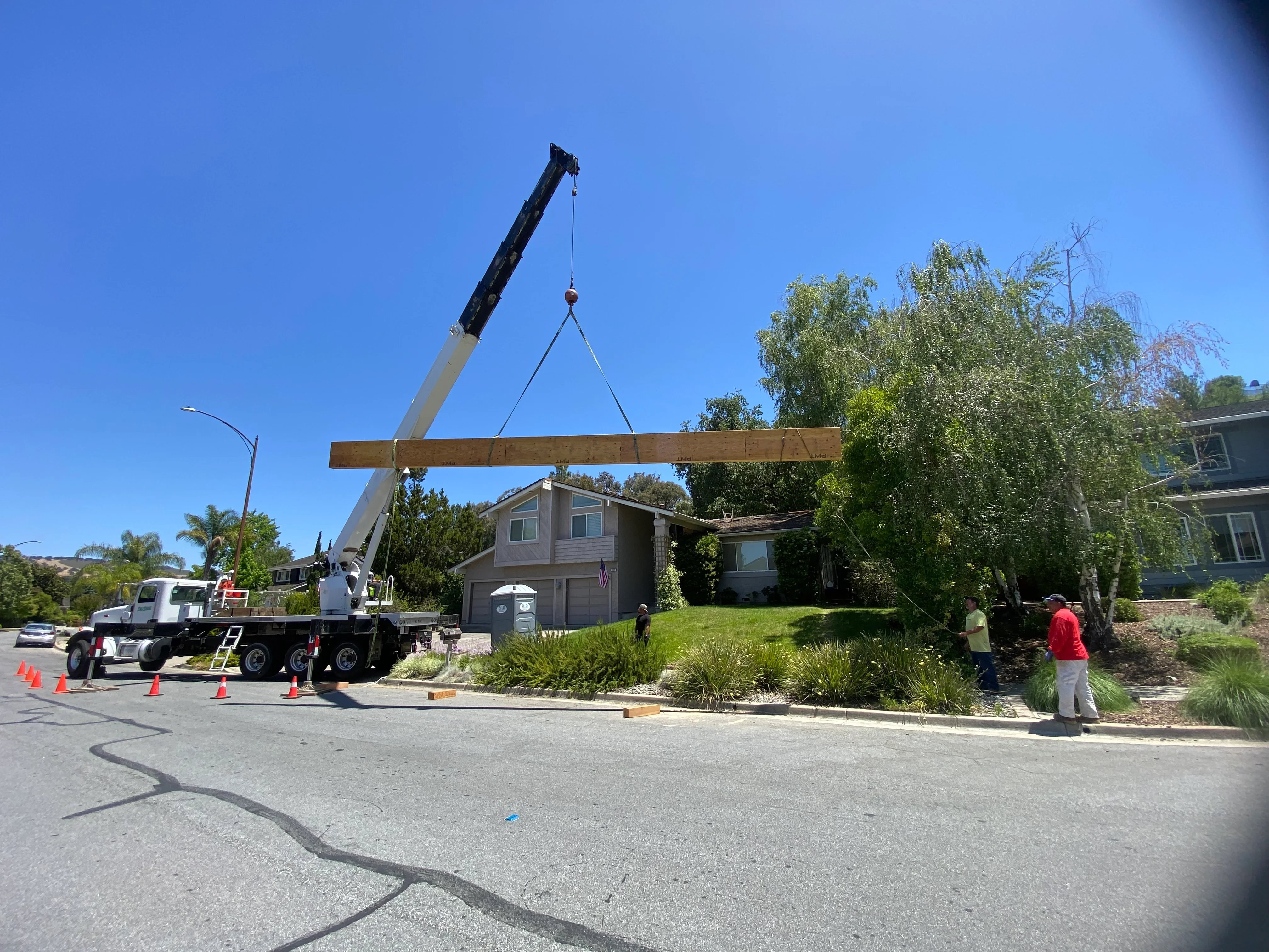 Mobile crane lifting wooden beam over residential home during construction