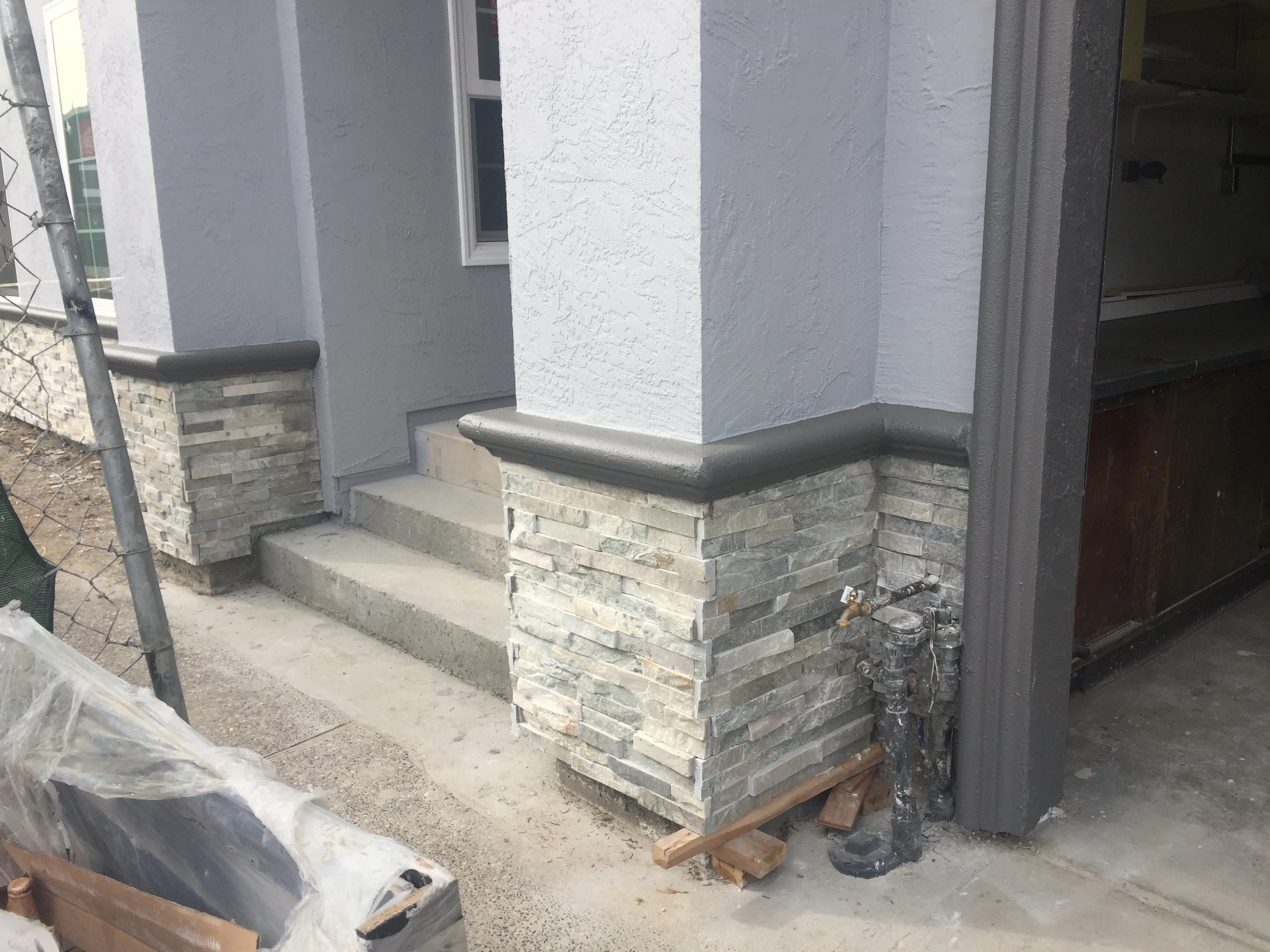 Stacked stone veneer base with concrete steps, black metal cap rail, and white stucco columns