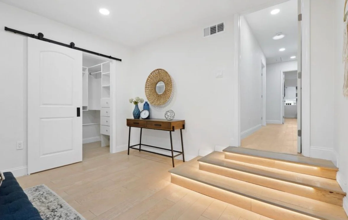 White sliding barn doors, recessed lighting, oak flooring, and built-in closet shelving in remodeled bedroom hallway