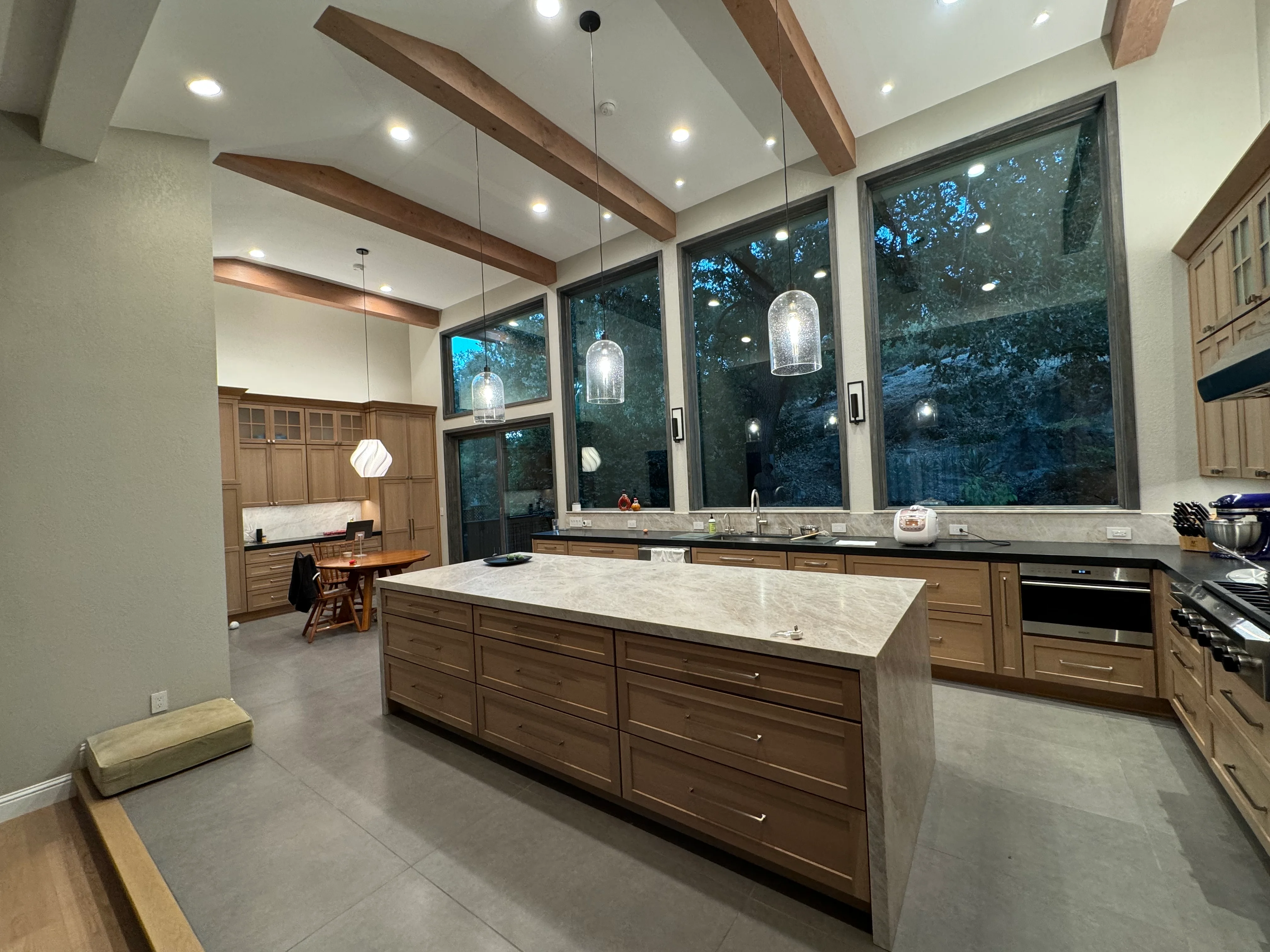 Modern kitchen with walnut cabinets, marble countertops, exposed wood beams, and large windows
