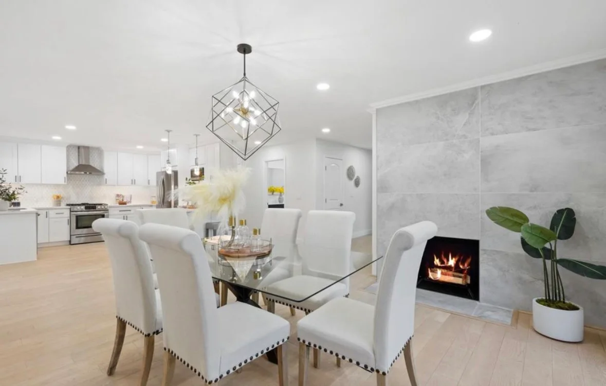 Modern kitchen and living room with white cabinets, fireplace, and geometric pendant lighting