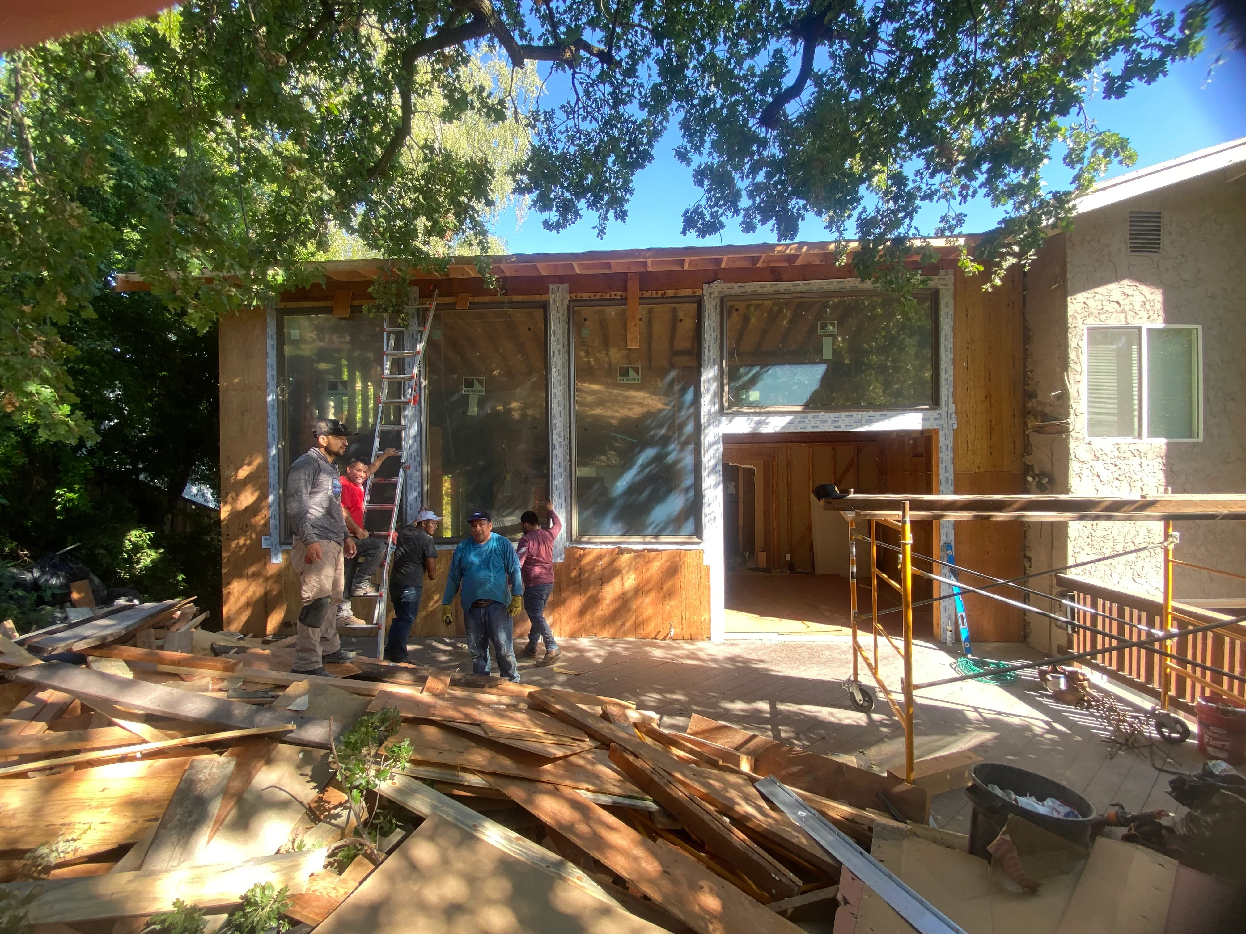 Residential addition under construction with wooden pergola, large windows, and metal deck railing