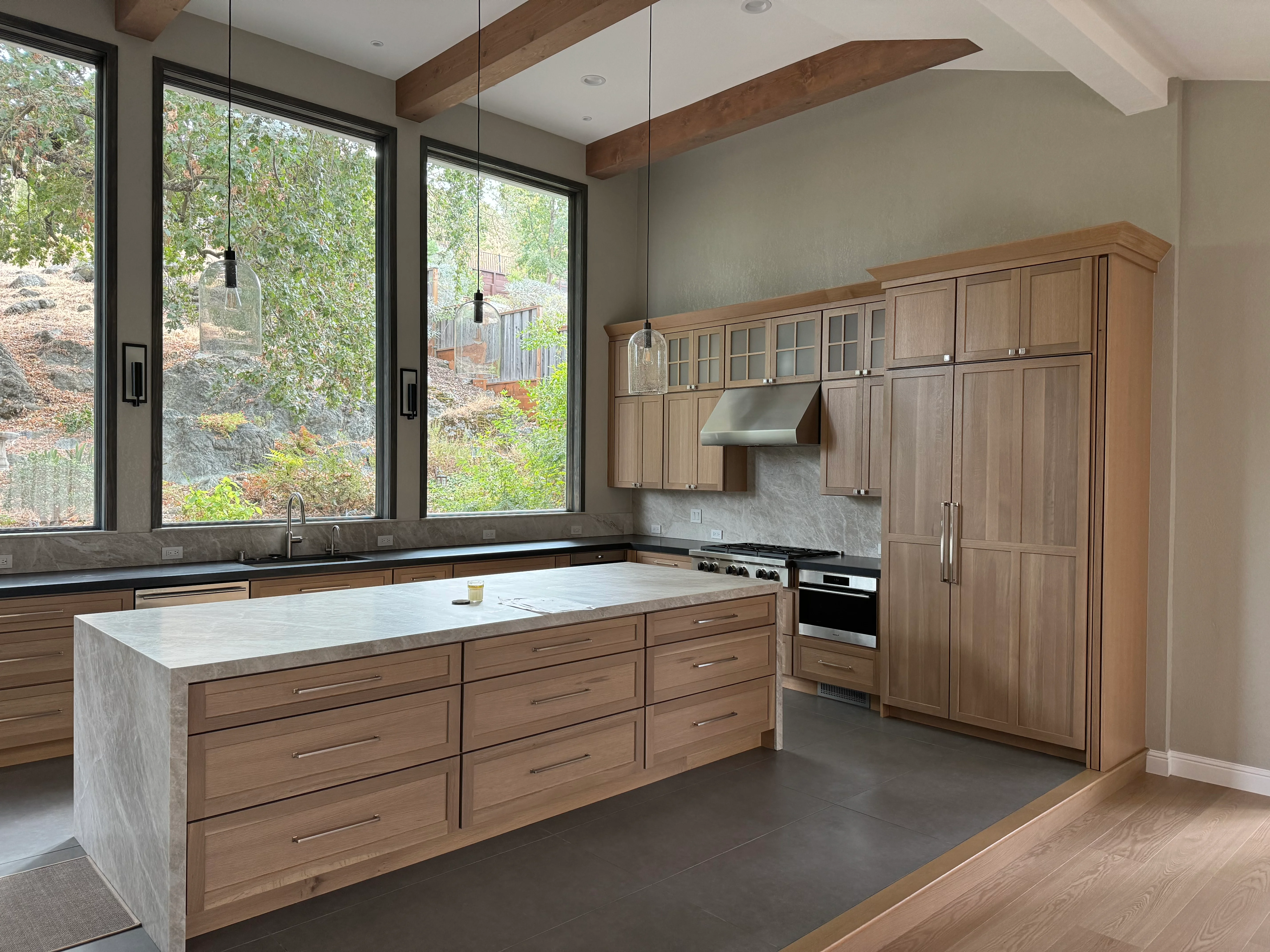 Modern kitchen with walnut cabinetry, marble island, stainless steel appliances, and large windows