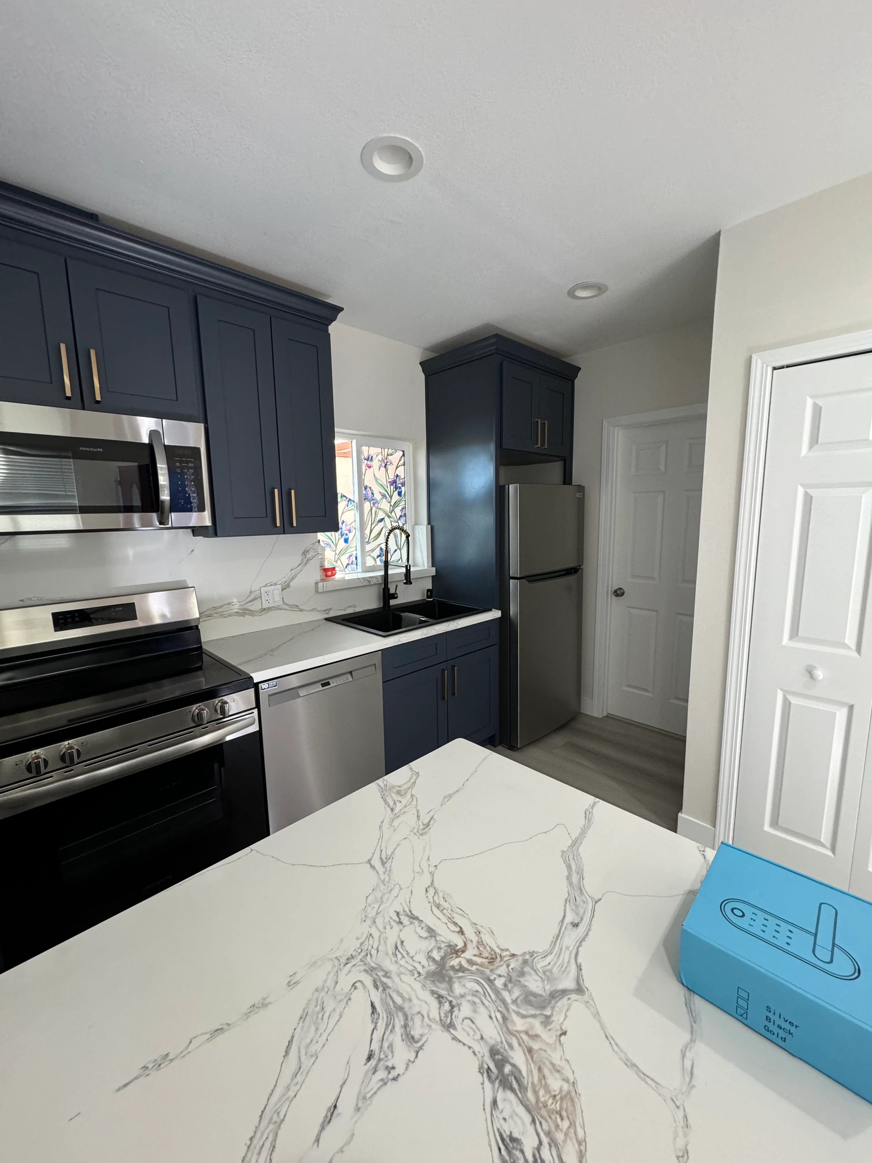 Navy cabinetry, white quartz countertops, stainless steel appliances, and recessed lighting in renovated kitchen