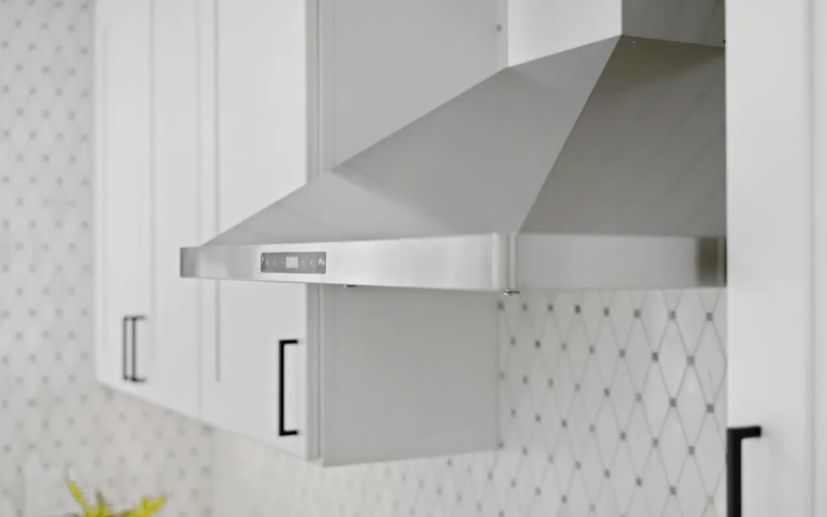 Stainless steel range hood with digital controls installed above white subway tile backsplash