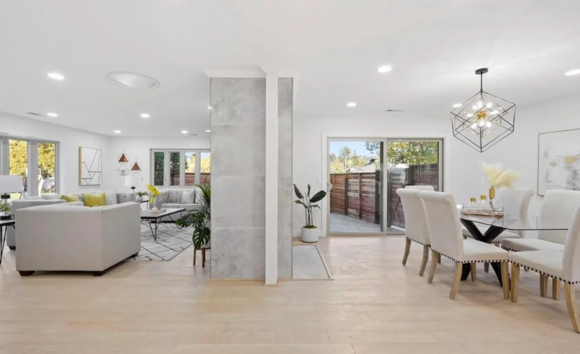 Open concept living room with light wood floors, white kitchen, marble columns, and modern pendant lighting