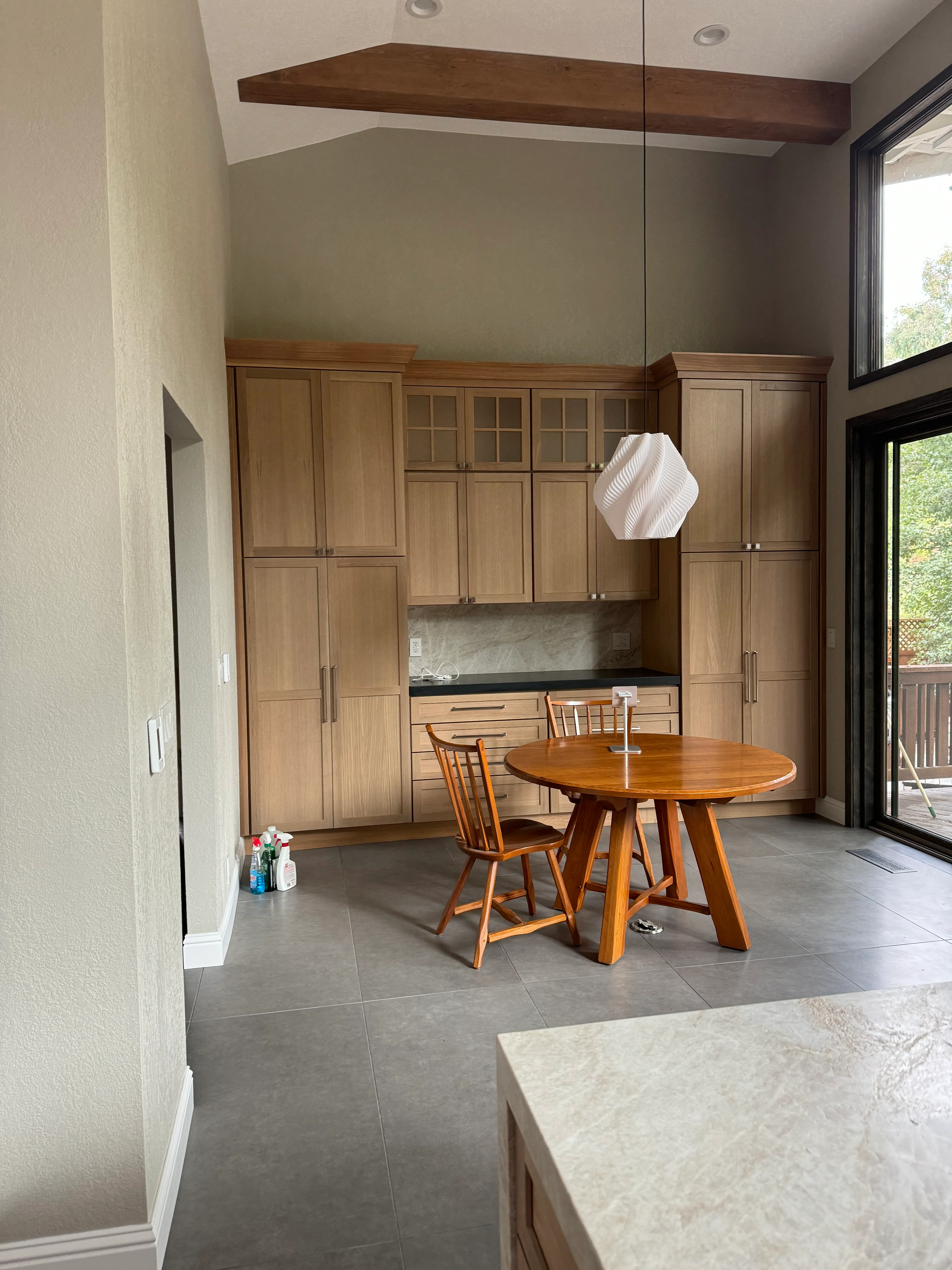 Custom wood kitchen cabinets with black countertop, marble backsplash, concrete flooring, and wood beam ceiling