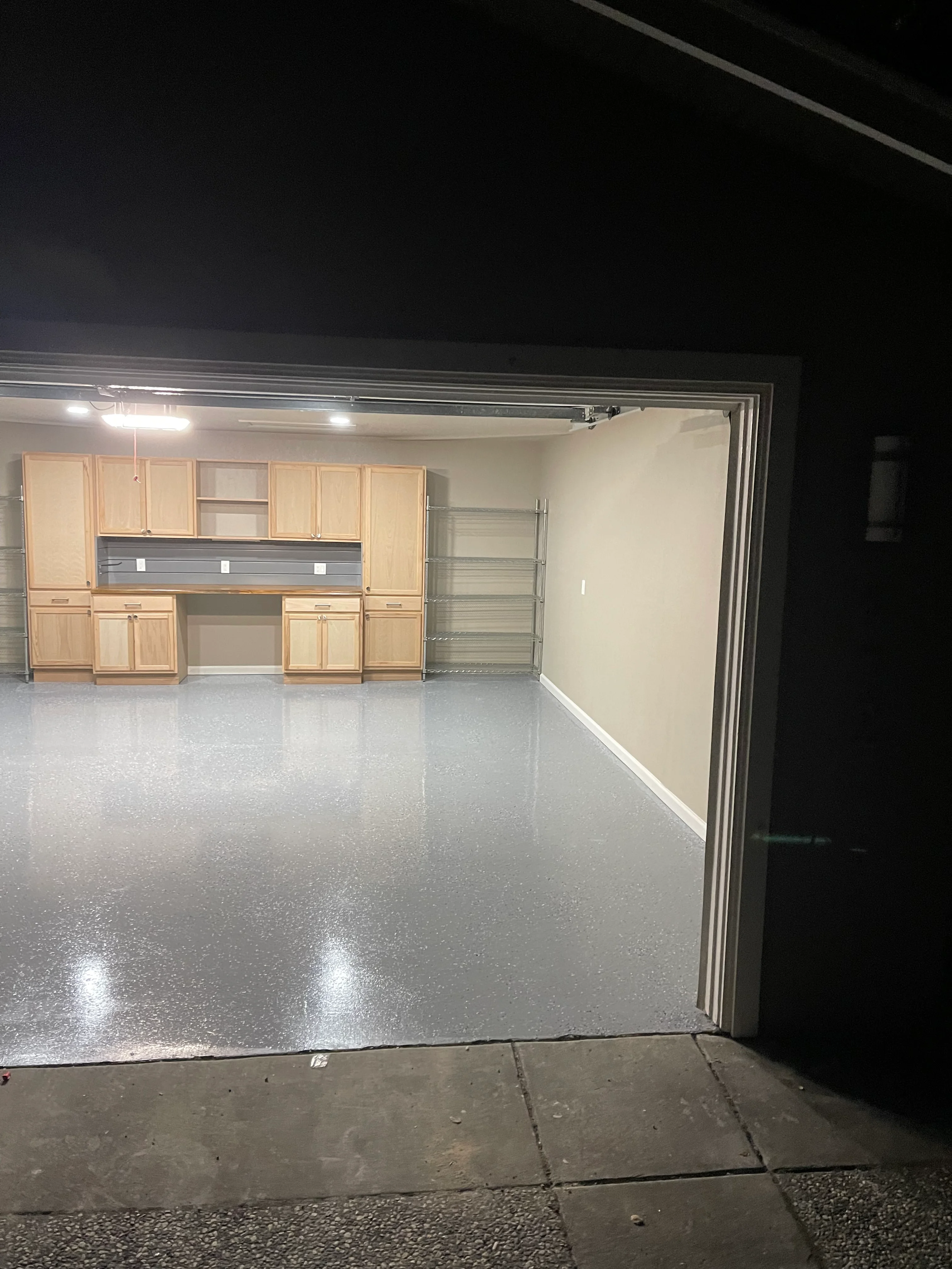Garage with gray speckled epoxy floor, wooden cabinetry, workbench, and LED lighting