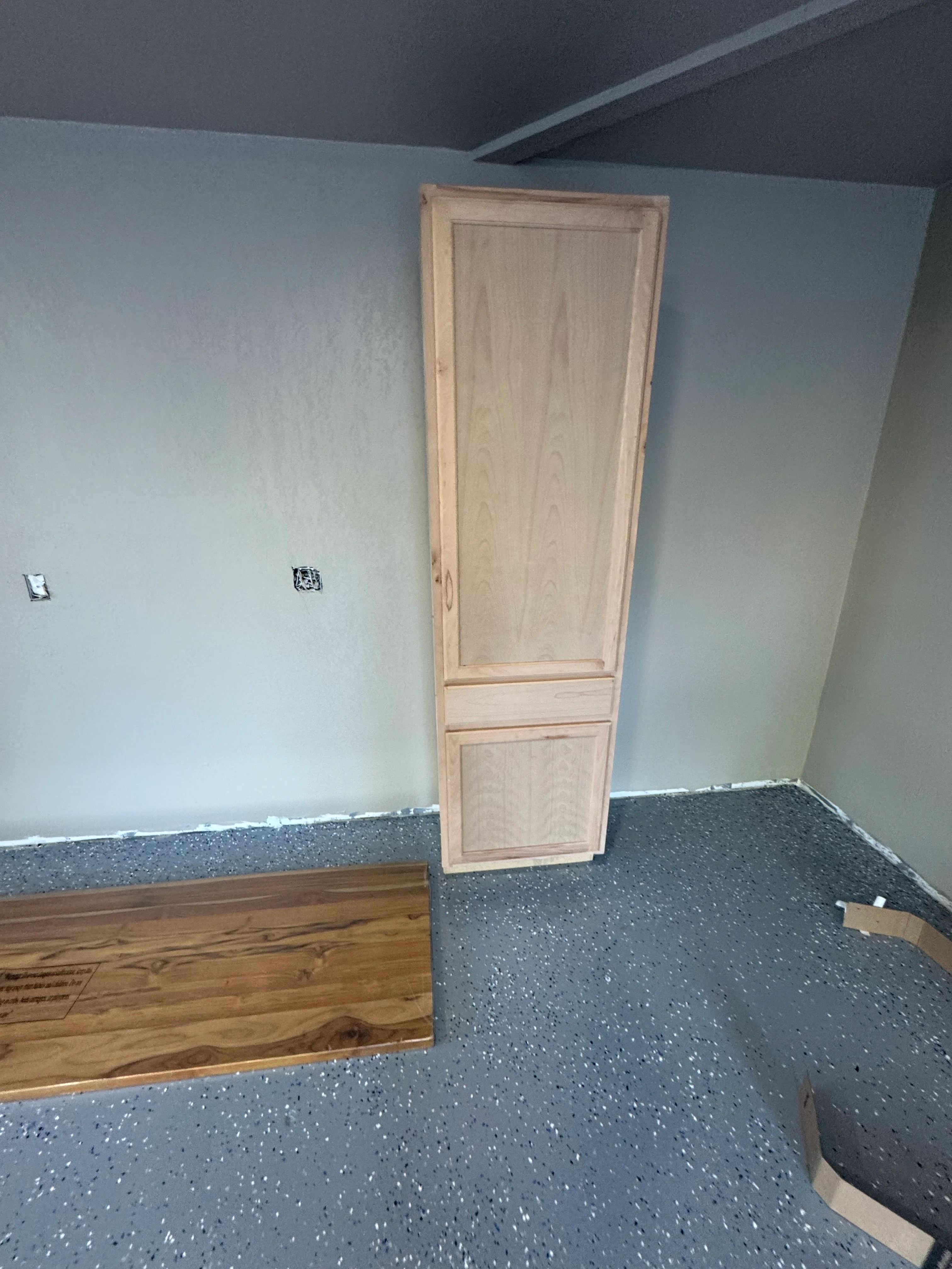 Custom wood cabinet installation with drywall walls and speckled epoxy flooring in interior remodel