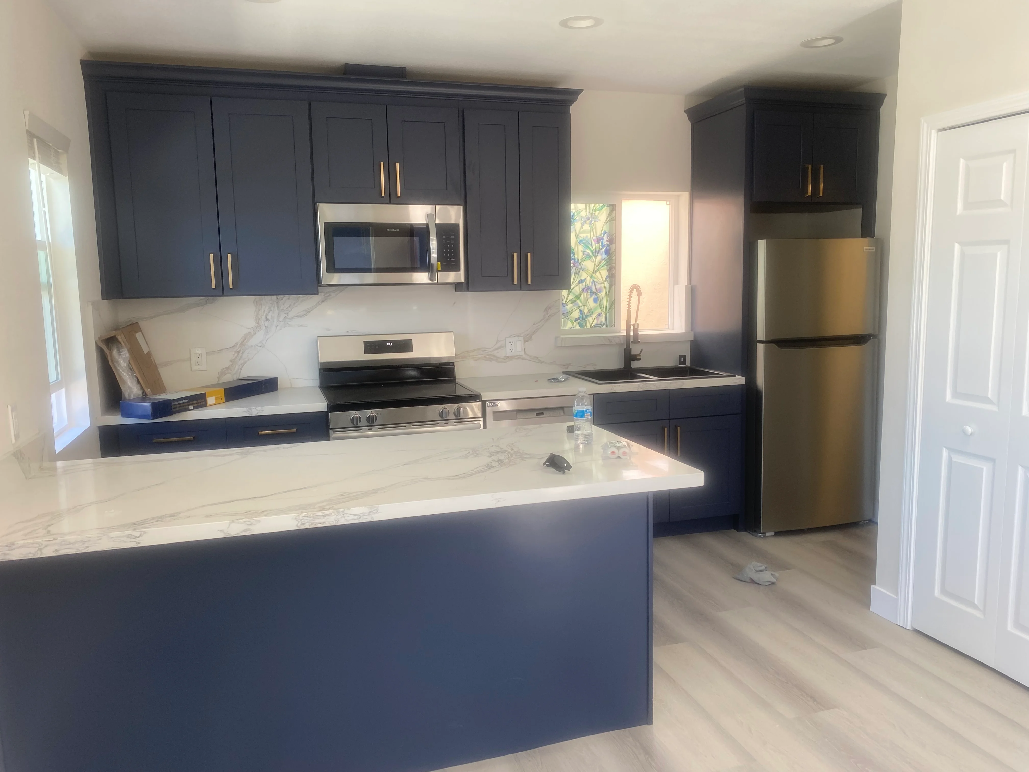 Navy cabinetry, marble countertops, stainless steel appliances, and waterfall island in modern kitchen