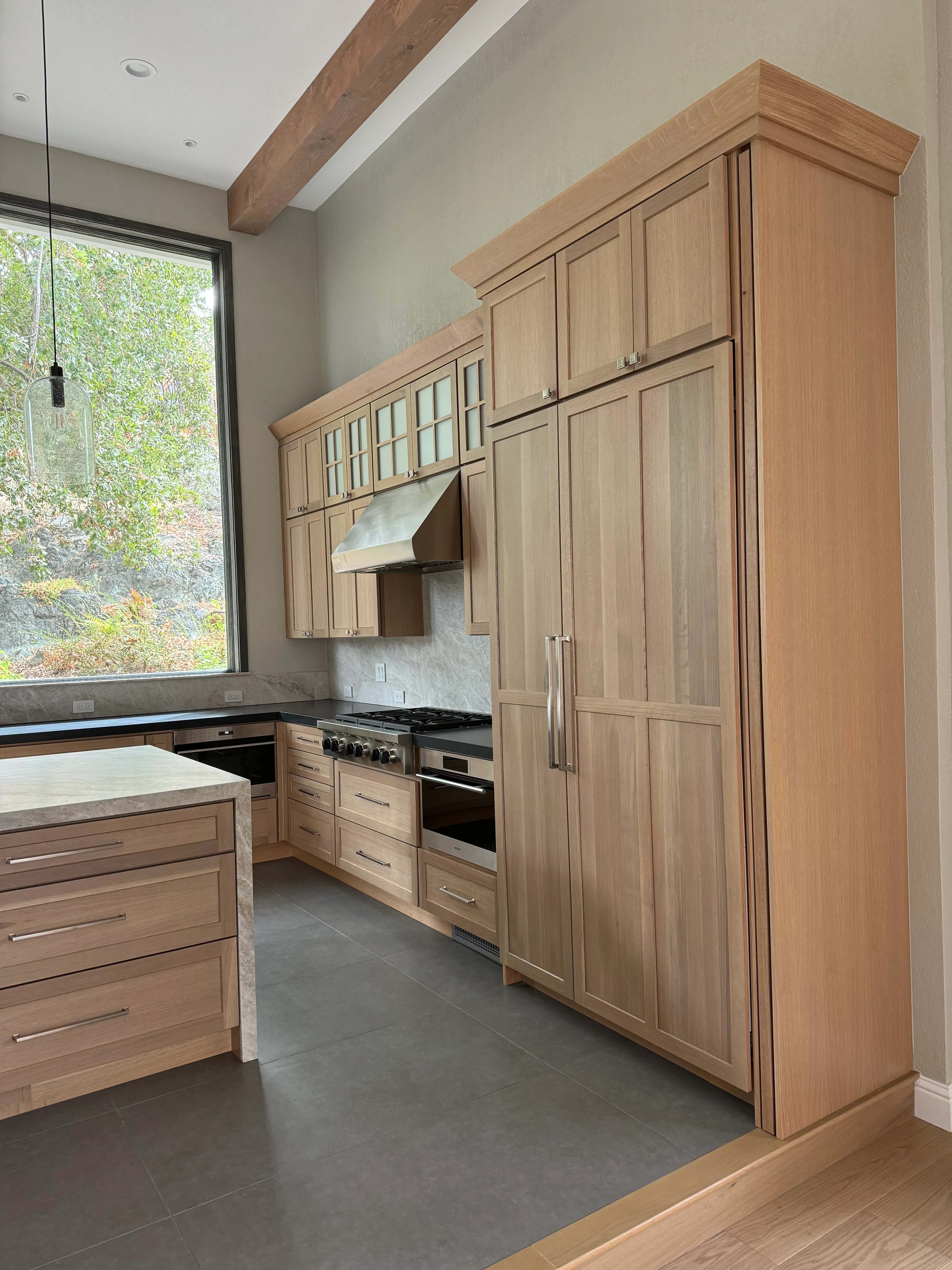 Light oak kitchen cabinets with stainless steel appliances, marble backsplash, and island with waterfall edge