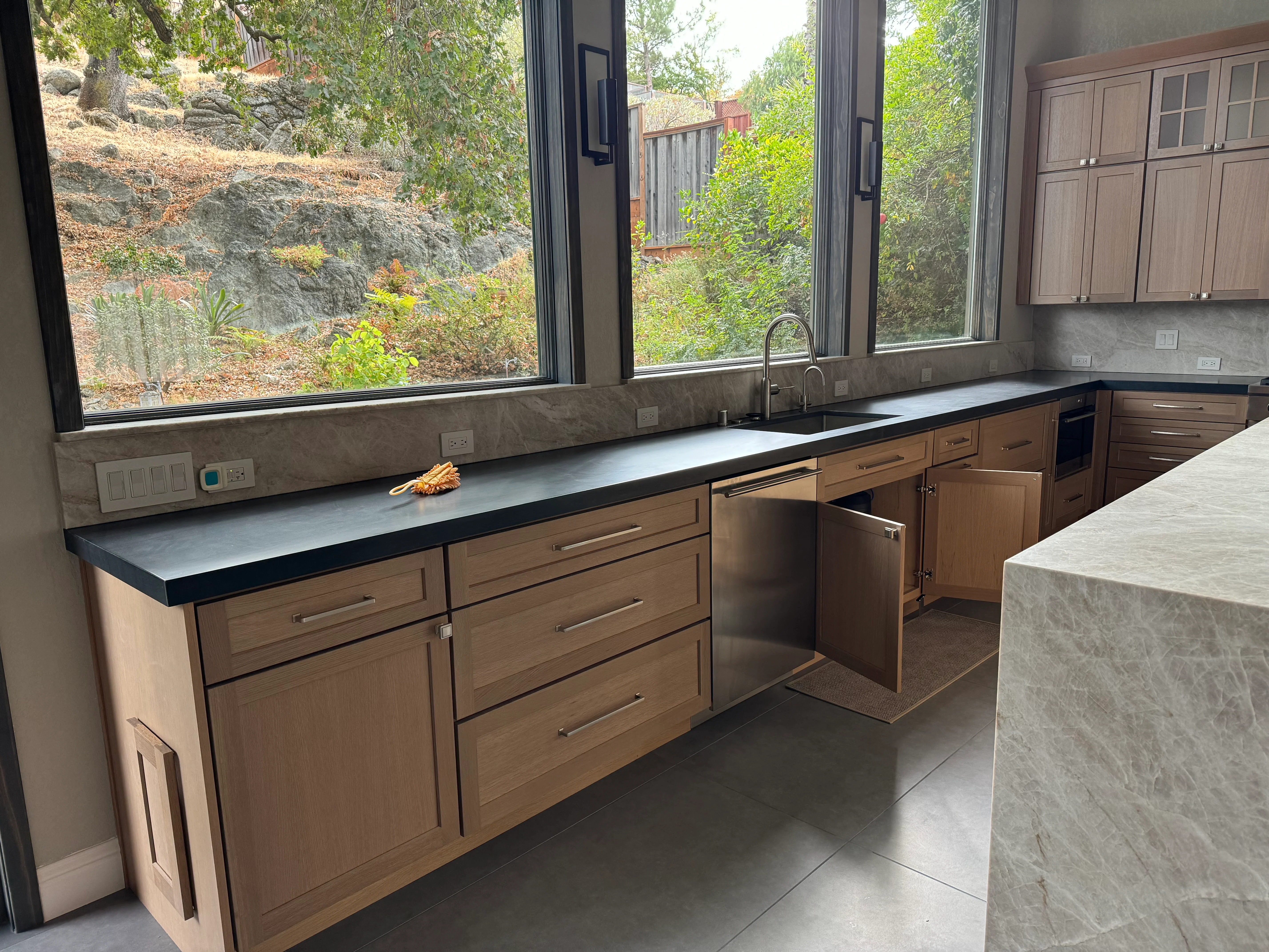 Kitchen with wood cabinets, black quartz counters, stainless appliances, and large windows