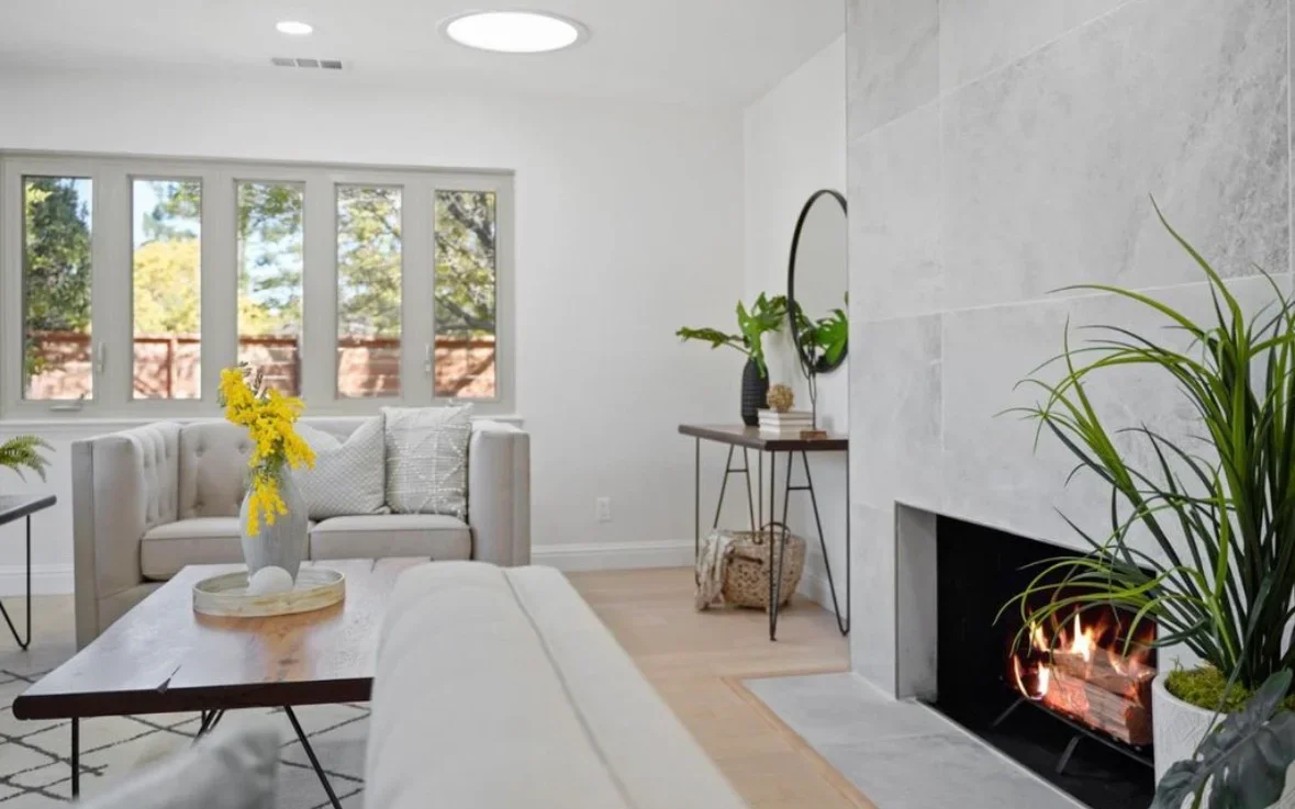 Modern living room with fireplace, gray sofa, hardwood floors, and large windows