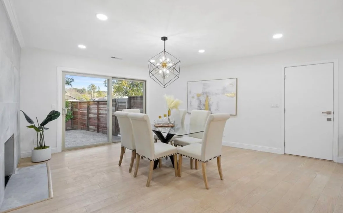 Open-concept living room with light wood floors, white walls, and glass sliding doors to patio