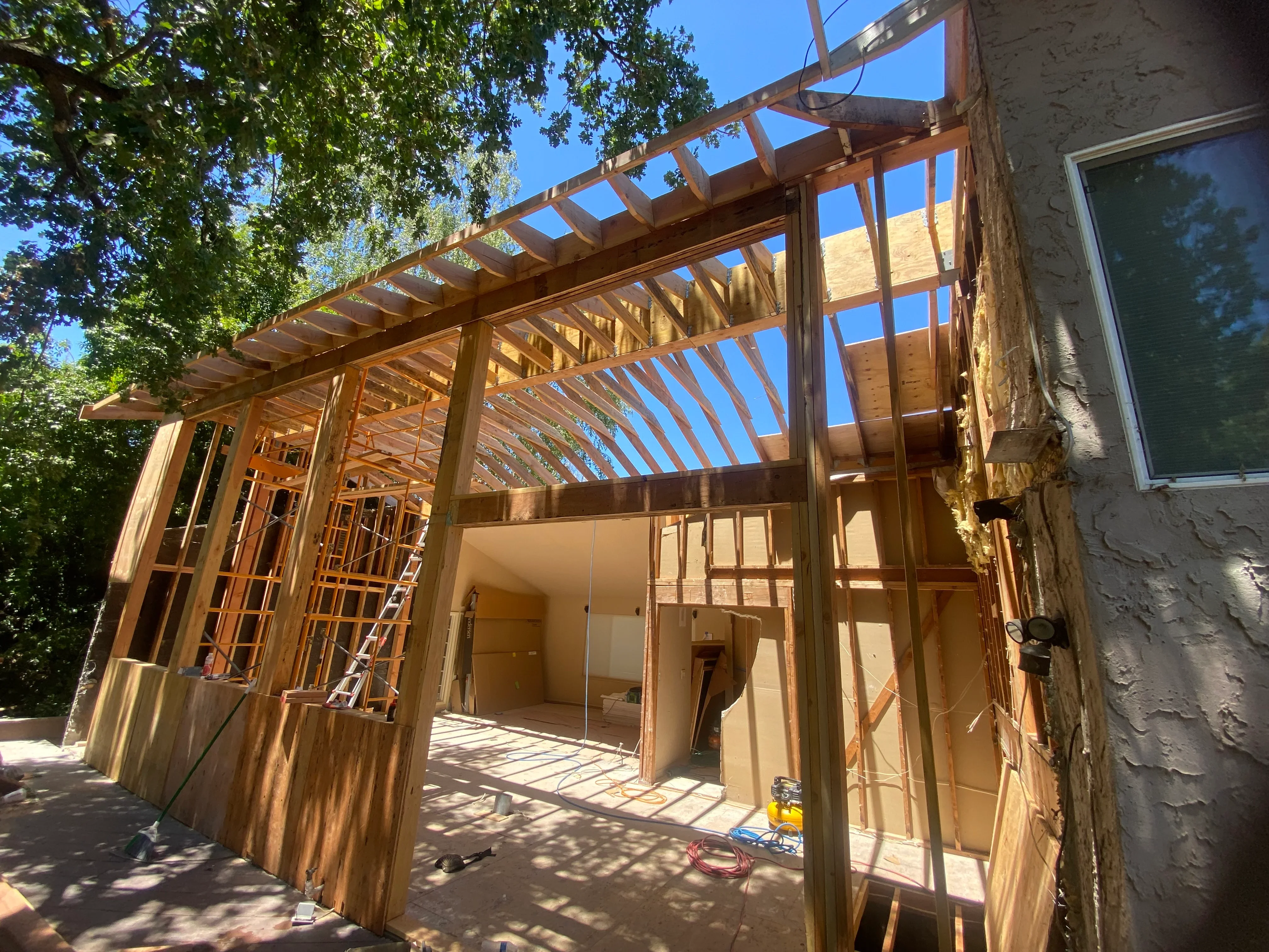 Wood-framed residential addition with pergola roof and large window openings under construction