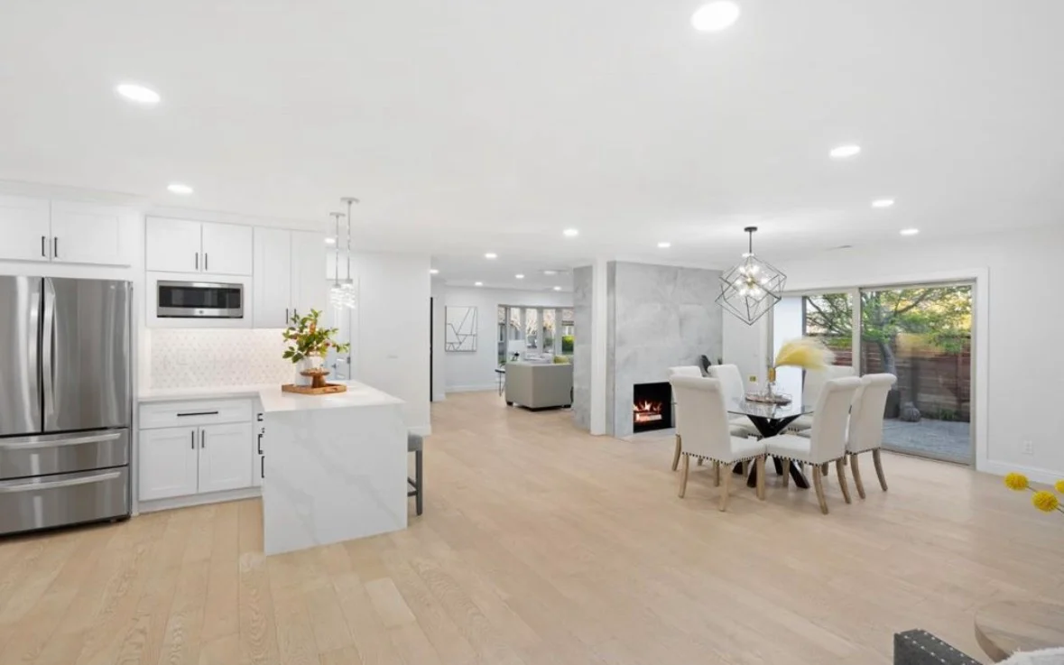 White kitchen with stainless steel appliances, island, and open living area with wood flooring