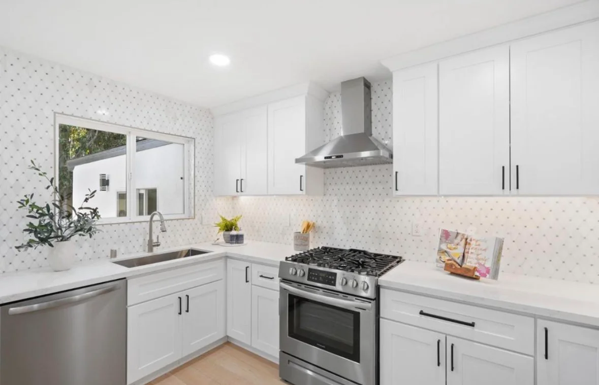 White kitchen with shaker cabinets, quartz counters, geometric tile backsplash, and stainless steel appliances