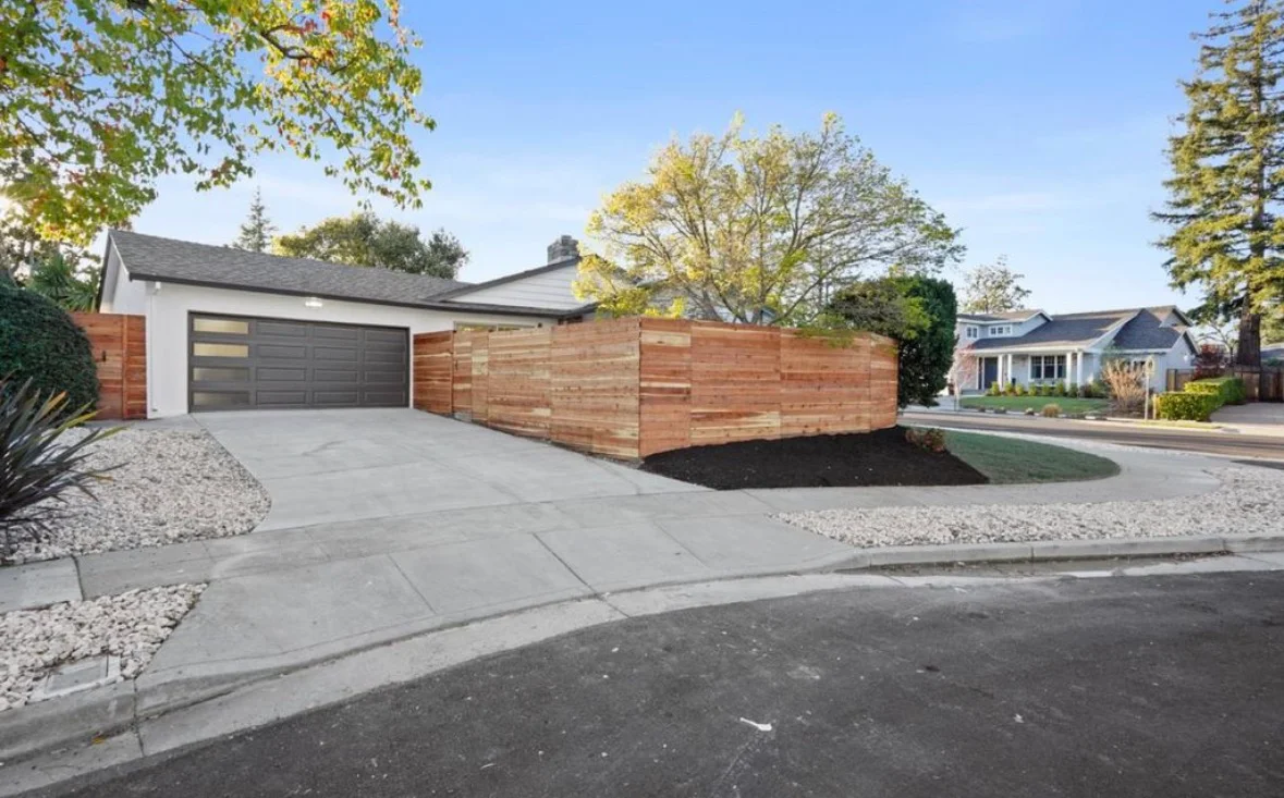 Concrete driveway, horizontal cedar fence, modern garage with dark panel doors, gravel landscaping