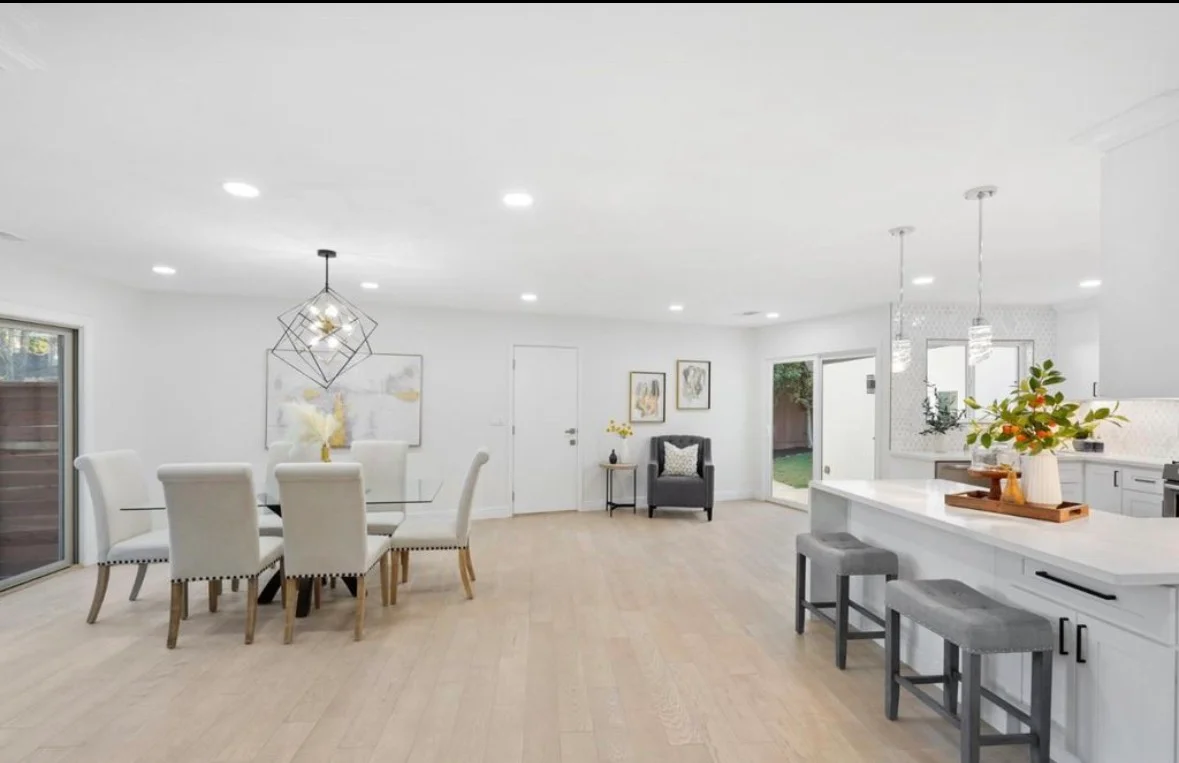 White kitchen with quartz counters, light wood floors, gray island seating, and open dining area