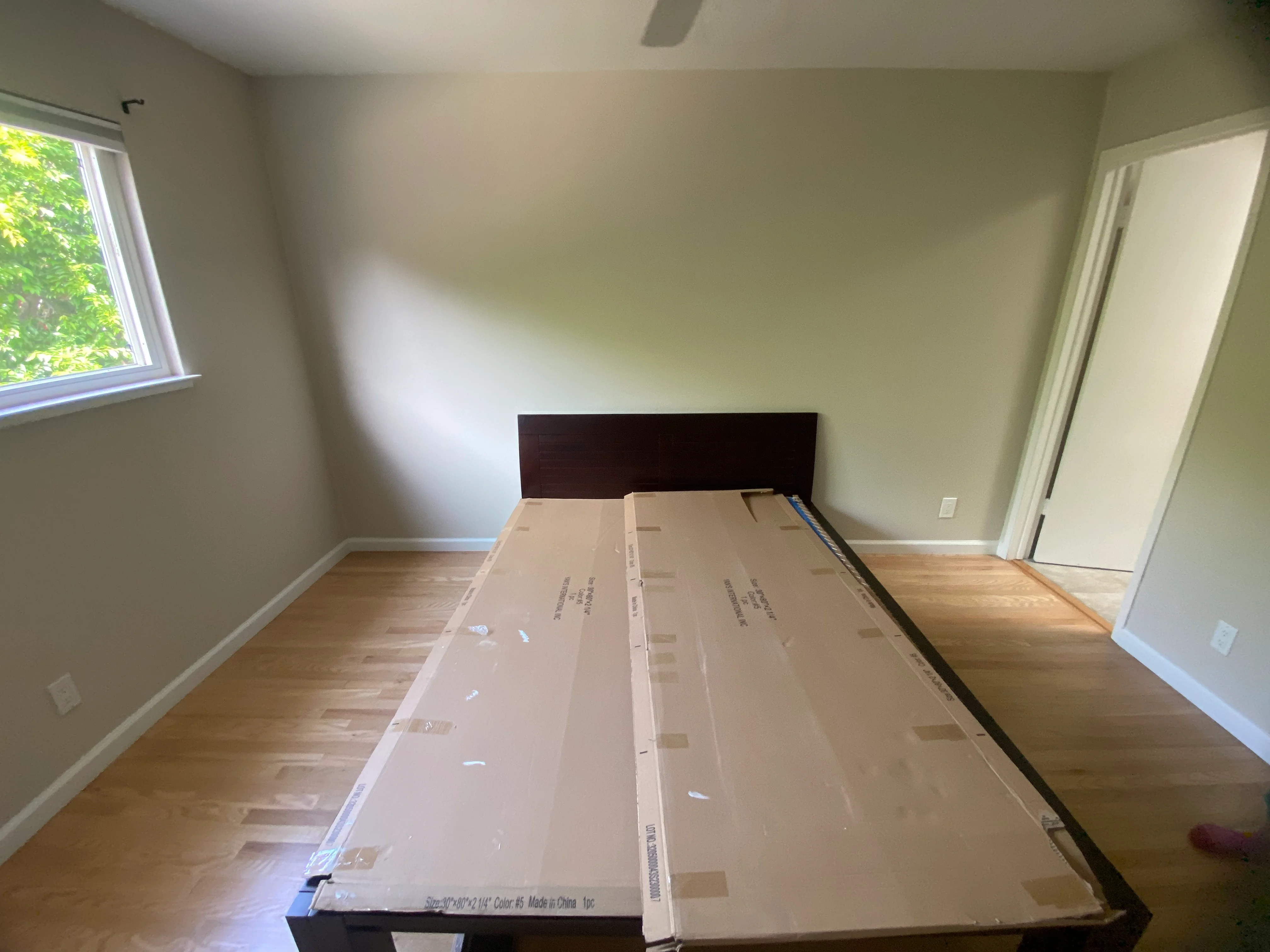 Hardwood flooring installation in progress with protective cardboard covering and dark wood bed frame