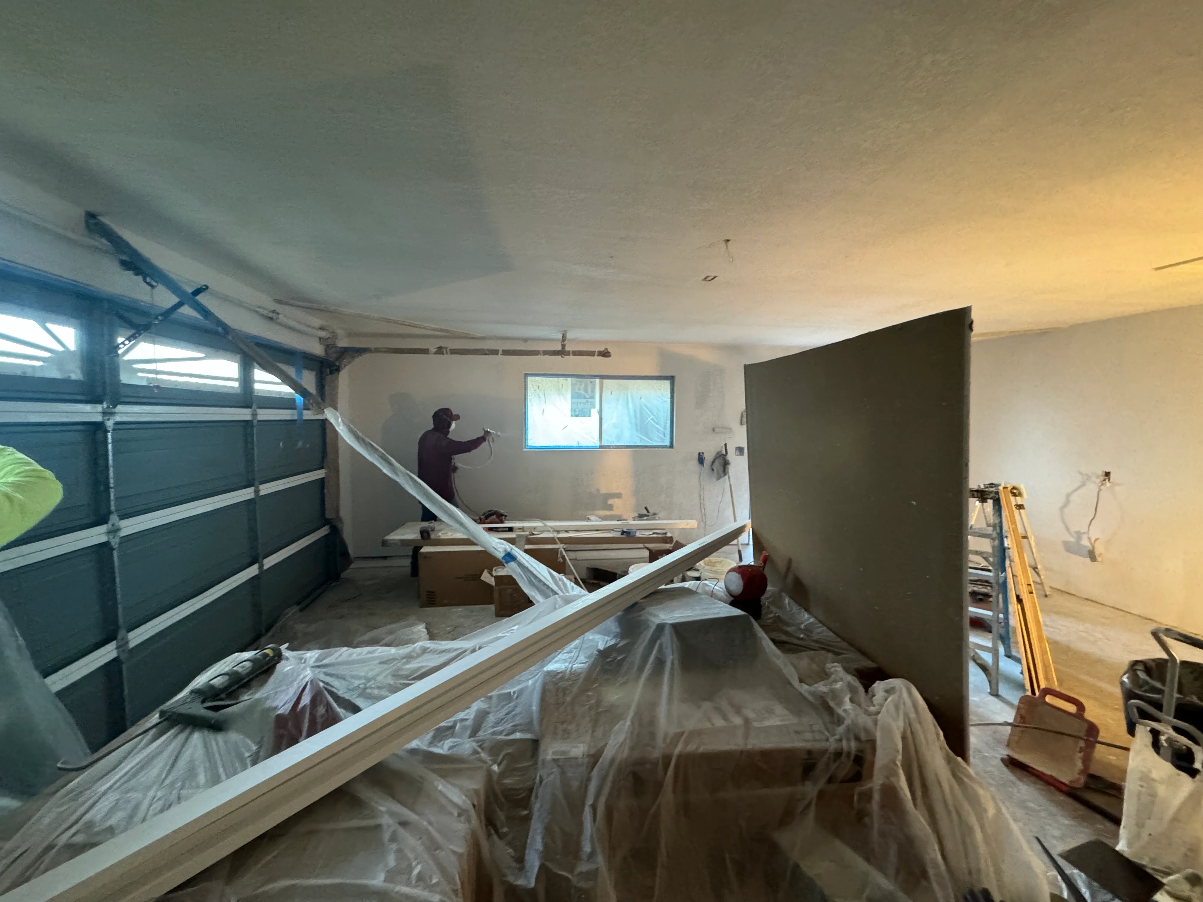 Garage interior with drywall, framing, new window, and protective plastic coverings during renovation