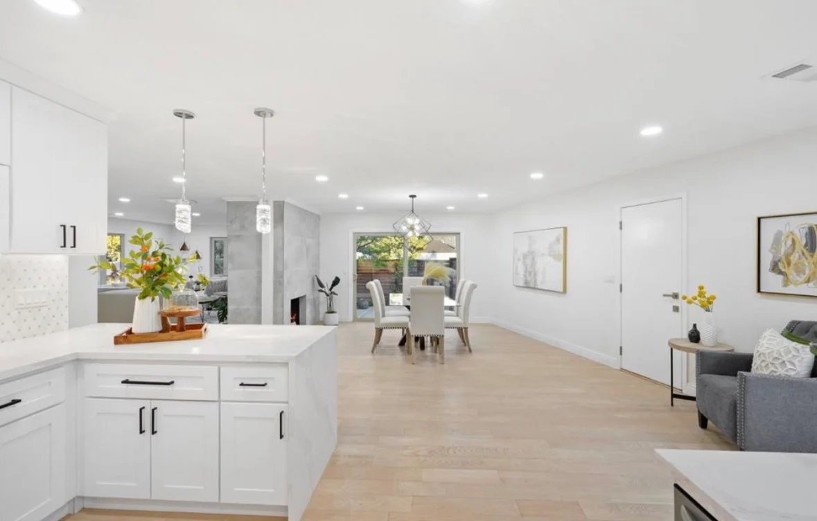 White kitchen with island, quartz counters, pendant lights, and open living space with wood flooring