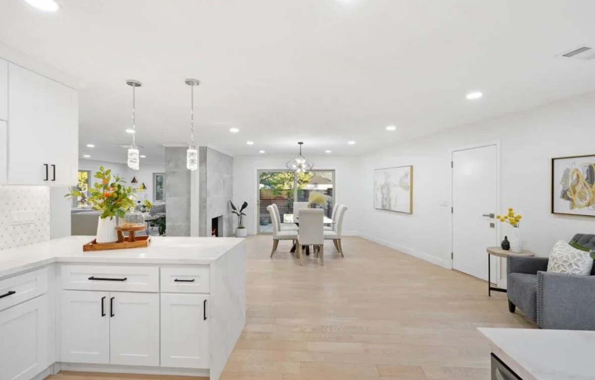 Modern white kitchen with island, pendant lights, and open floor plan connecting to dining area
