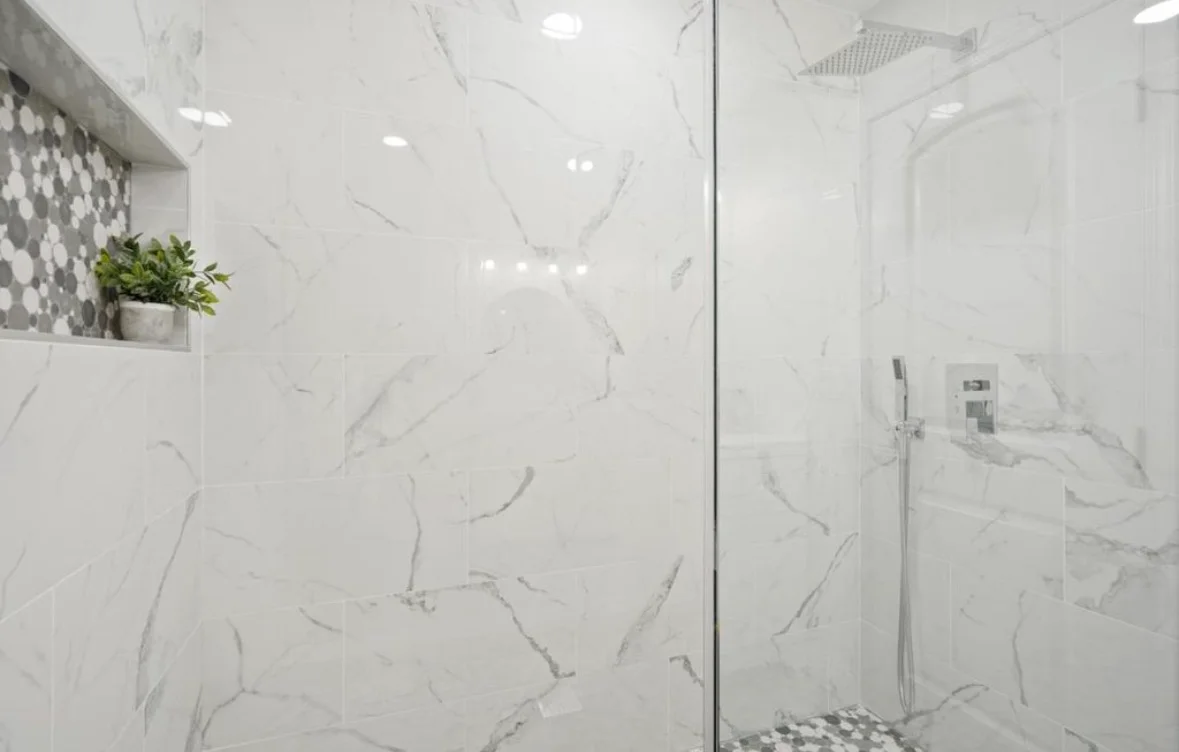 Marble-look tile shower with frameless glass enclosure and custom niche with hexagonal accent tiles