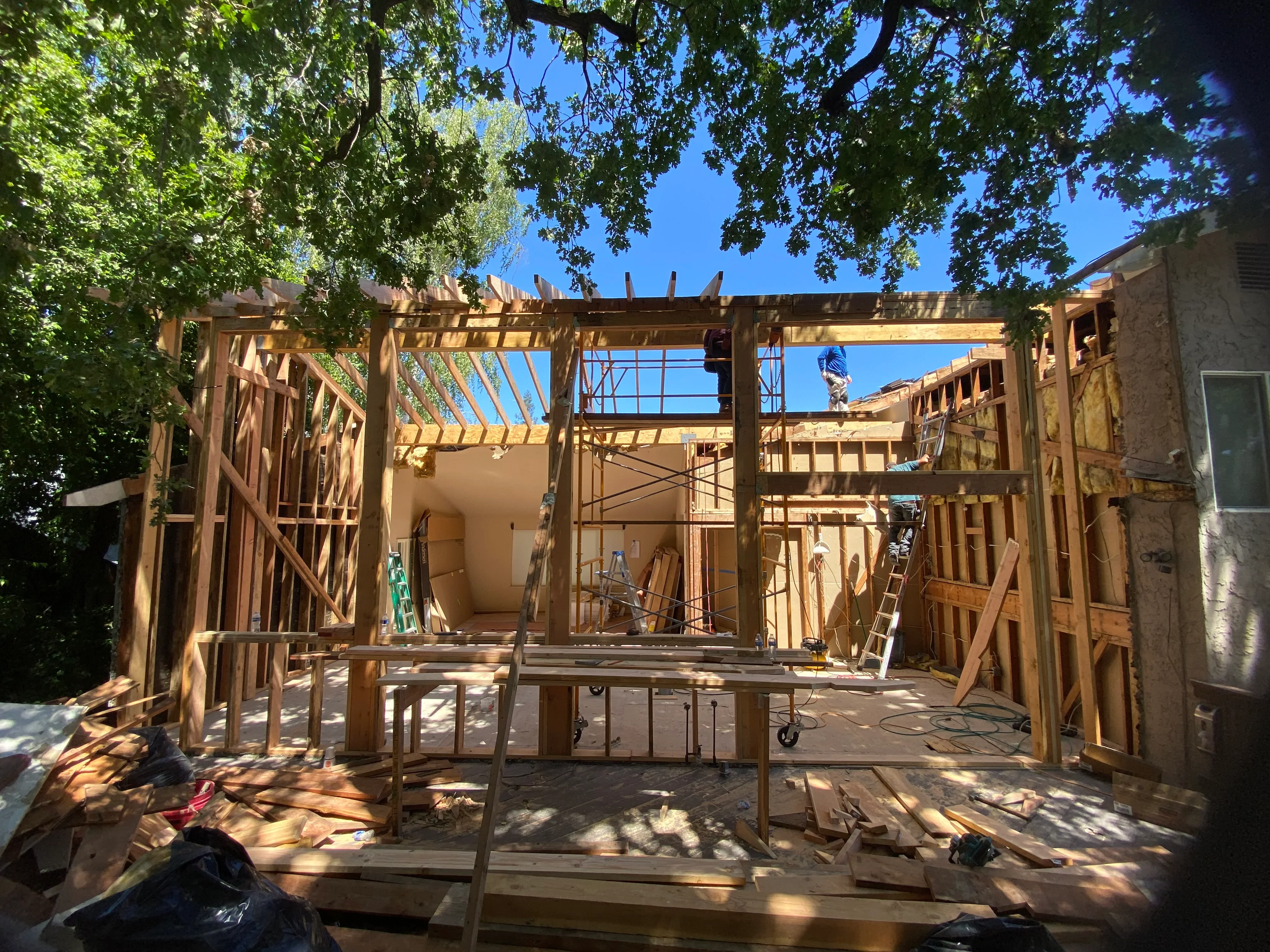 Wood-framed residential addition under construction with exposed studs and roof trusses