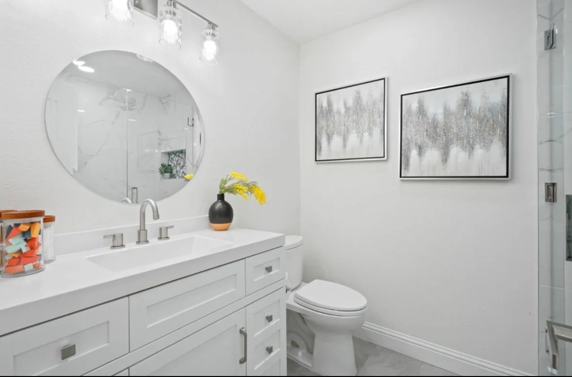 White bathroom vanity with quartz countertop, round mirror, and subway tile wainscoting