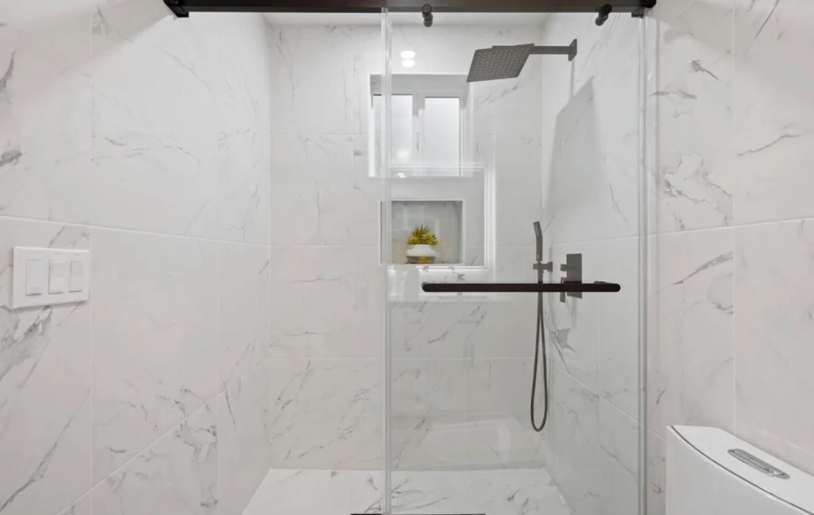 White marble tile bathroom with frameless glass shower, black fixtures, and recessed niche