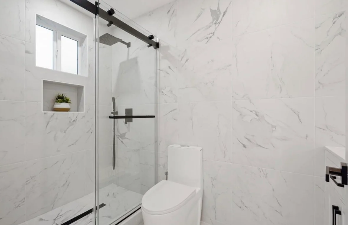 Marble tile bathroom with frameless glass shower, black fixtures, and recessed niche