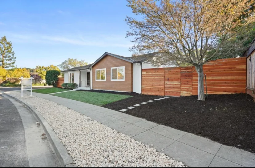Modern home with brown composite siding, white windows, horizontal wood fence, and landscaped yard with gravel and mulch