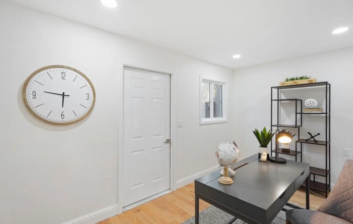 Modern office with white walls, recessed lighting, wood flooring, black metal shelving, and dark desk