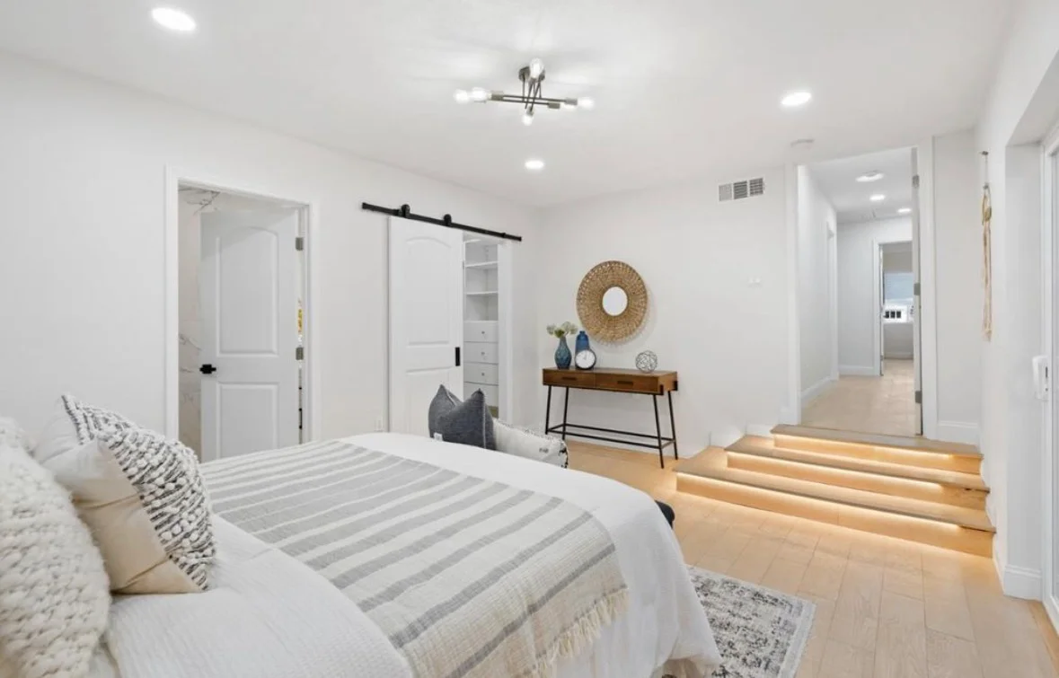Bright primary bedroom with white walls, wood flooring, recessed lighting, and black barn door closet