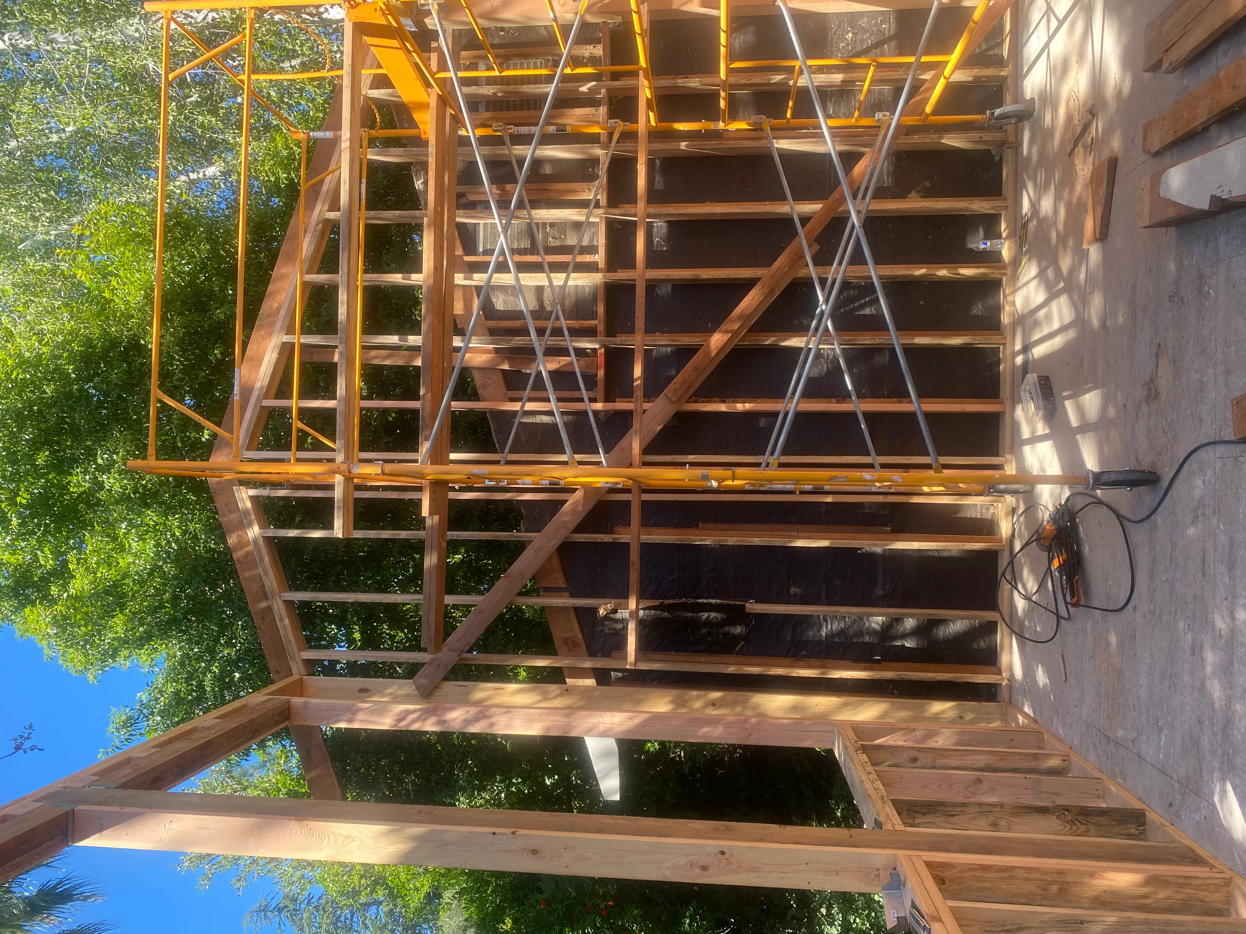 Wooden framing structure with yellow scaffolding and metal cross-bracing during residential construction