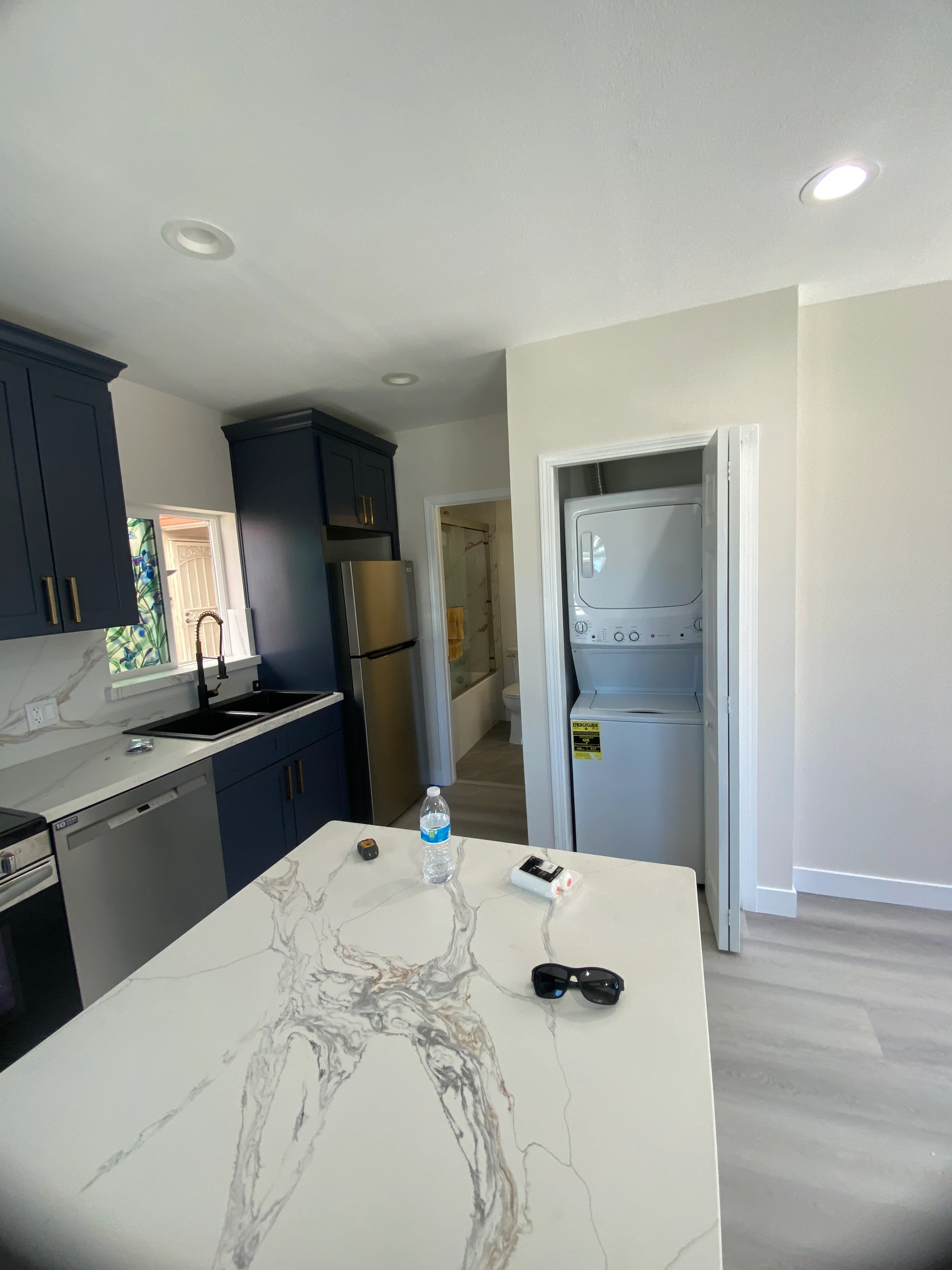 Modern kitchen with navy cabinets, white quartz counters, stainless steel appliances, and integrated laundry closet