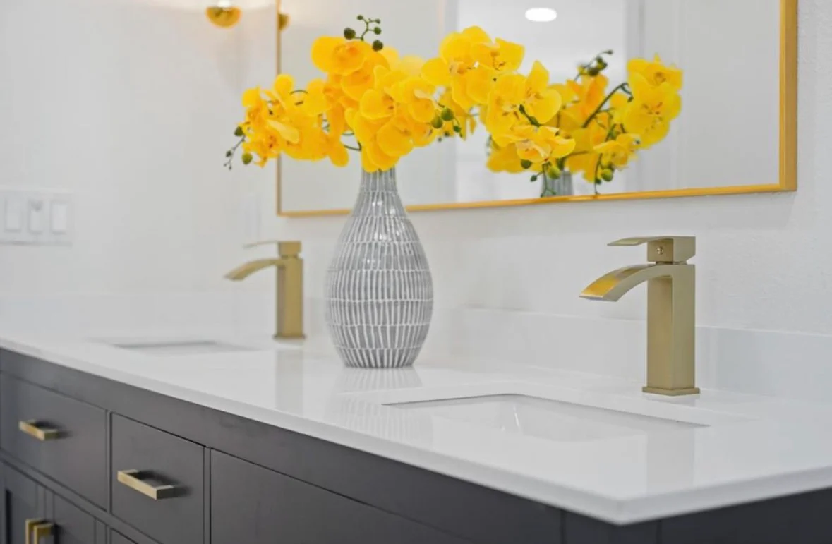 Modern bathroom vanity with white quartz countertop, gray cabinetry, and gold faucets