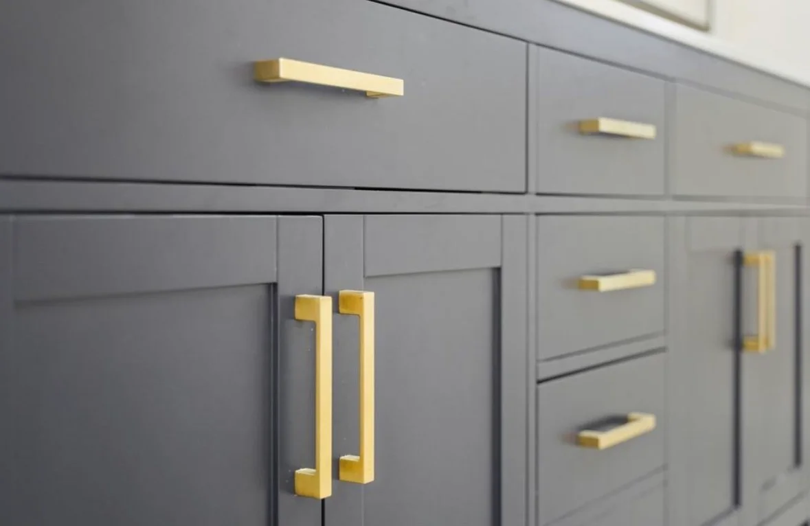 Gray kitchen cabinets with brass pulls and handles, recessed panel doors
