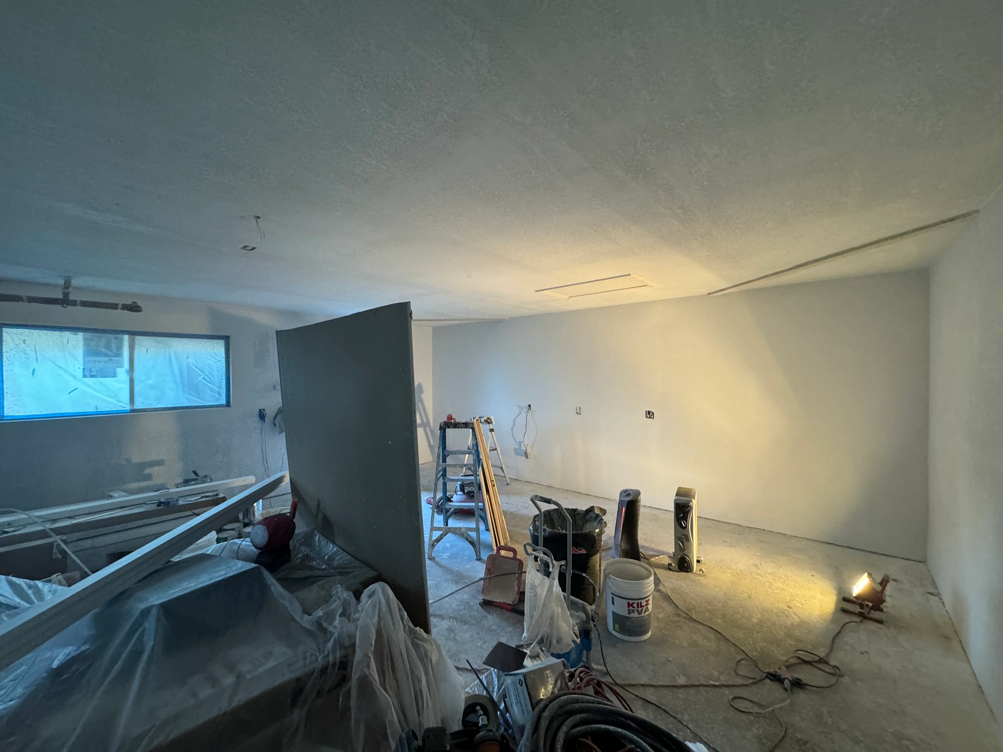 Interior drywall installation with recessed ceiling lights, primed walls ready for paint